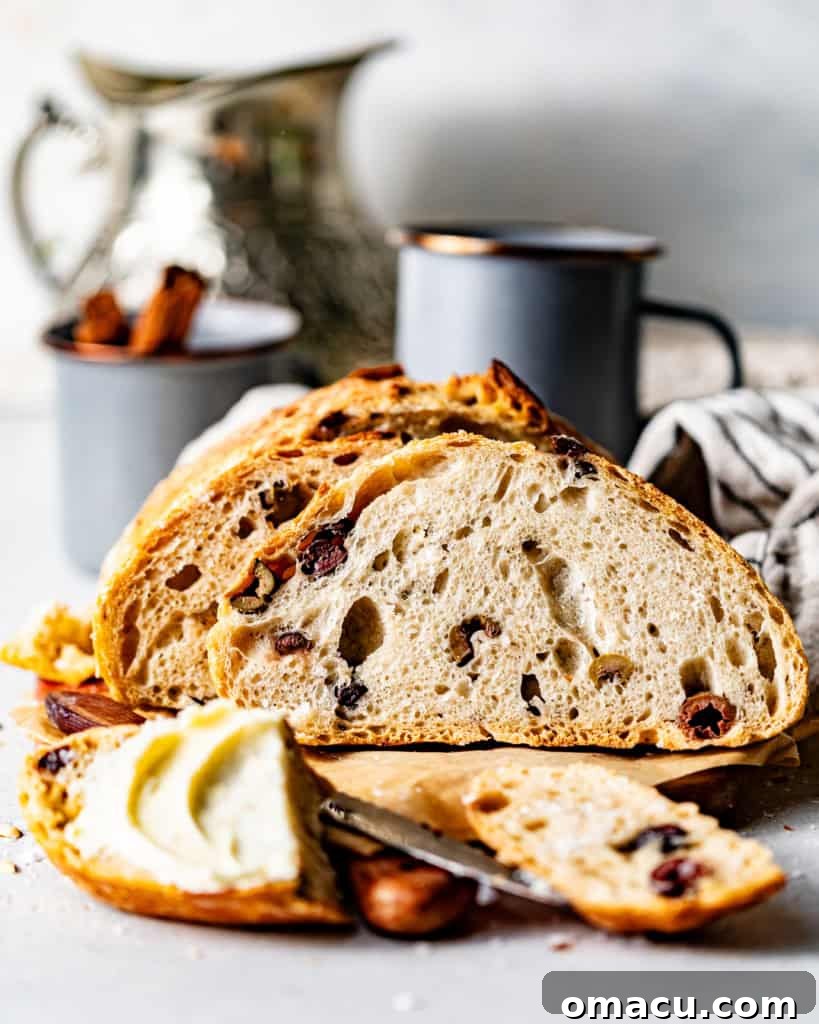 Sliced no-knead olive bread on a wooden cutting board with a piece topped with butter, highlighting its crispy crust and tender crumb.