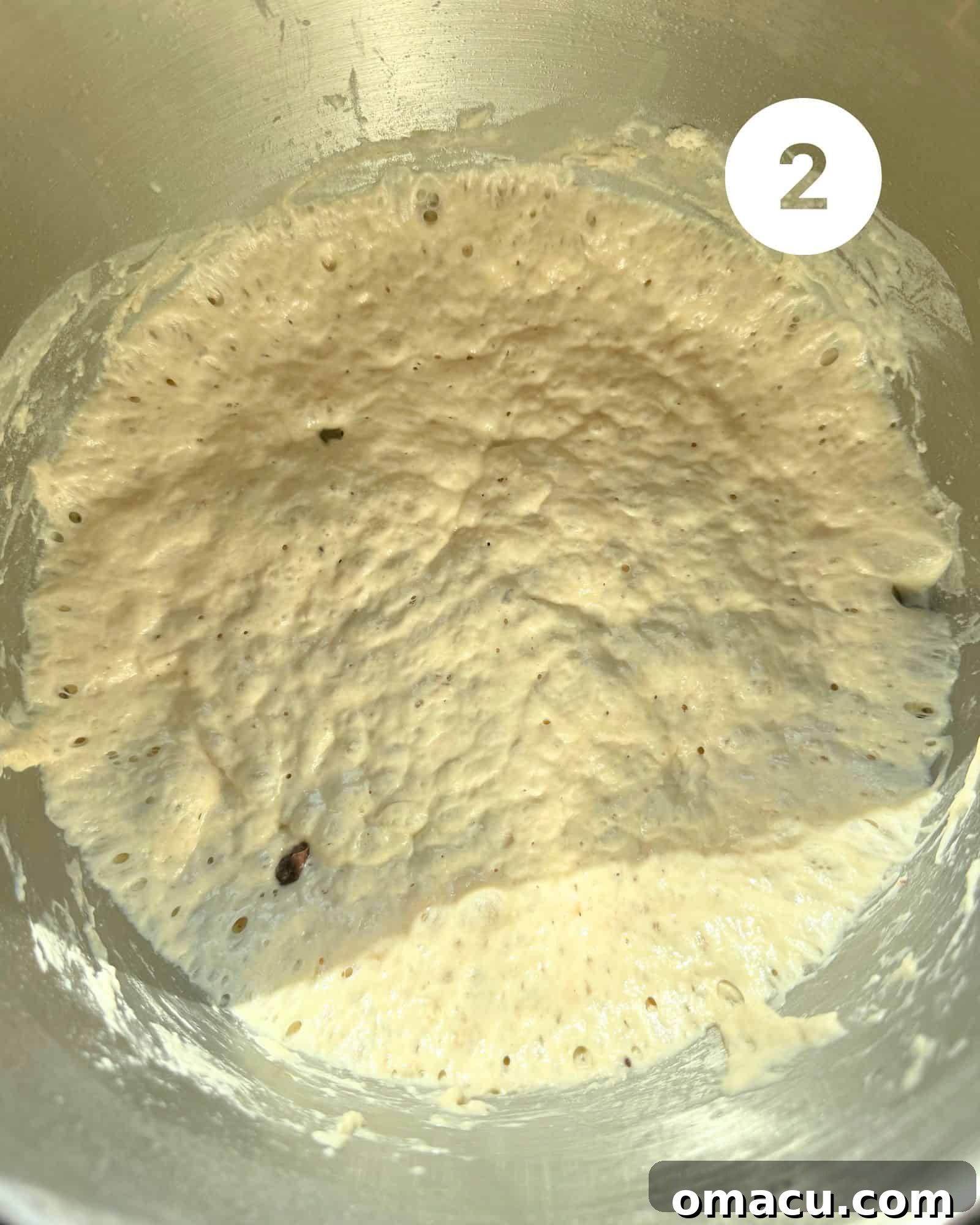 Risen dough in a bowl, showing air bubbles, with olives, salt, and rosemary sprinkled on top before mixing.