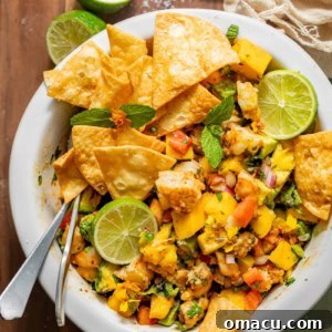 mango shrimp salad in a white bowl garnished with tortilla chips and limes.