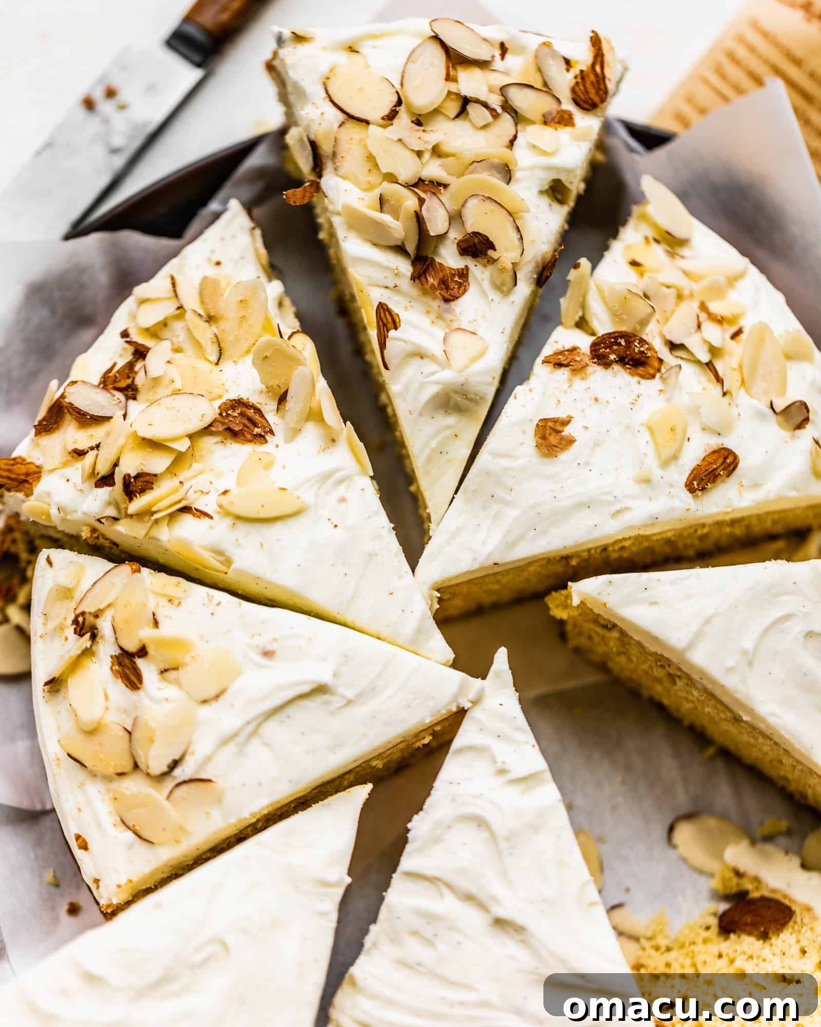 A freshly baked and frosted almond cake, beautifully sliced and arranged on a serving tray, garnished with additional sliced almonds.