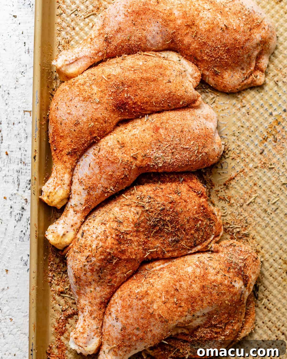 Seasoned chicken leg quarters laid out on a baking tray, ready for the next step in the cooking process.
