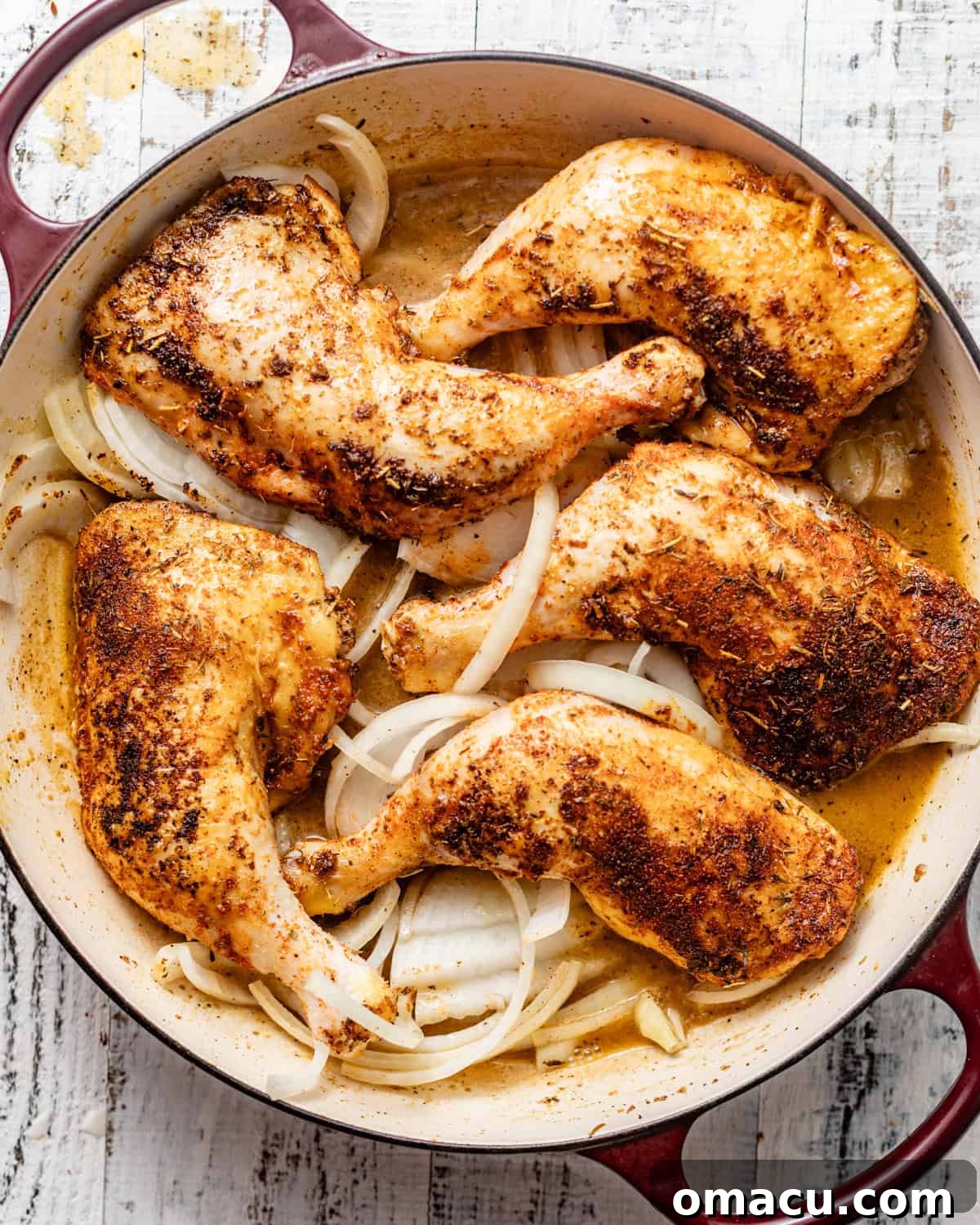 Seared chicken leg quarters and sliced onions returned to the skillet with the pan sauce, covered and ready for baking.