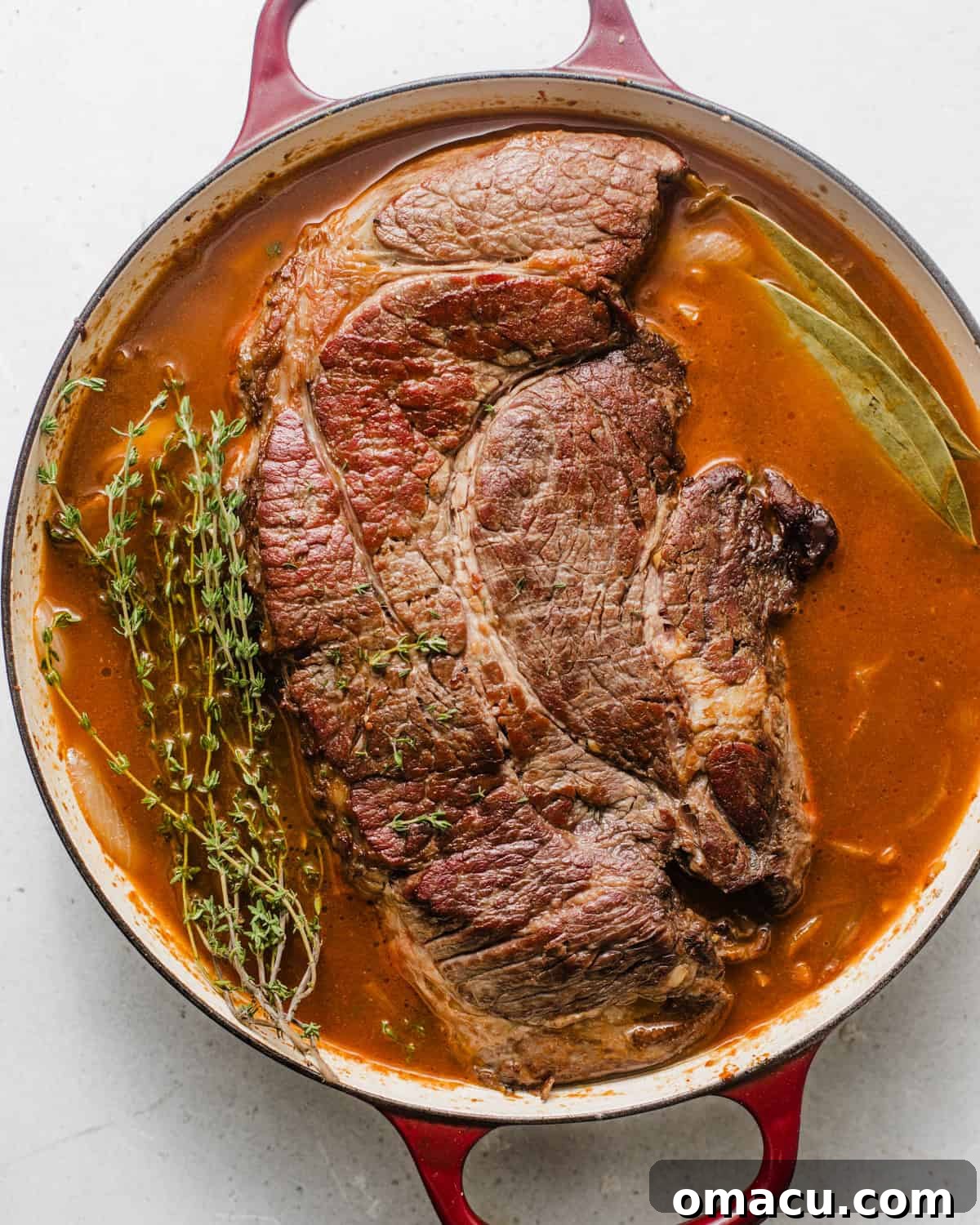 chuck roast in the pot with thyme, caramelized onions, whiskey, red wine, and bay leaves. 