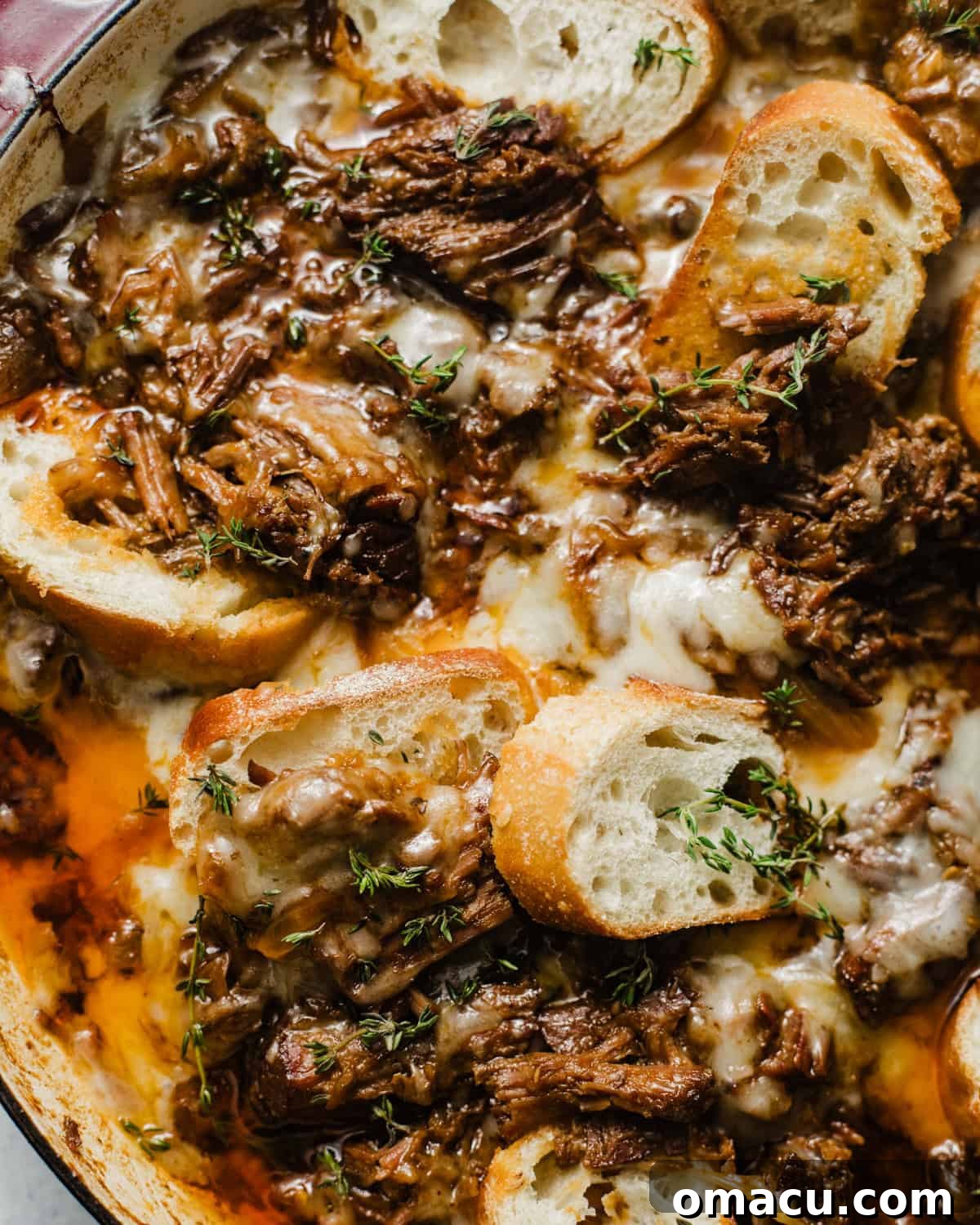 up close photo of french onion pot roast in a braising pan topped with gruyere cheese and sliced baguettes.