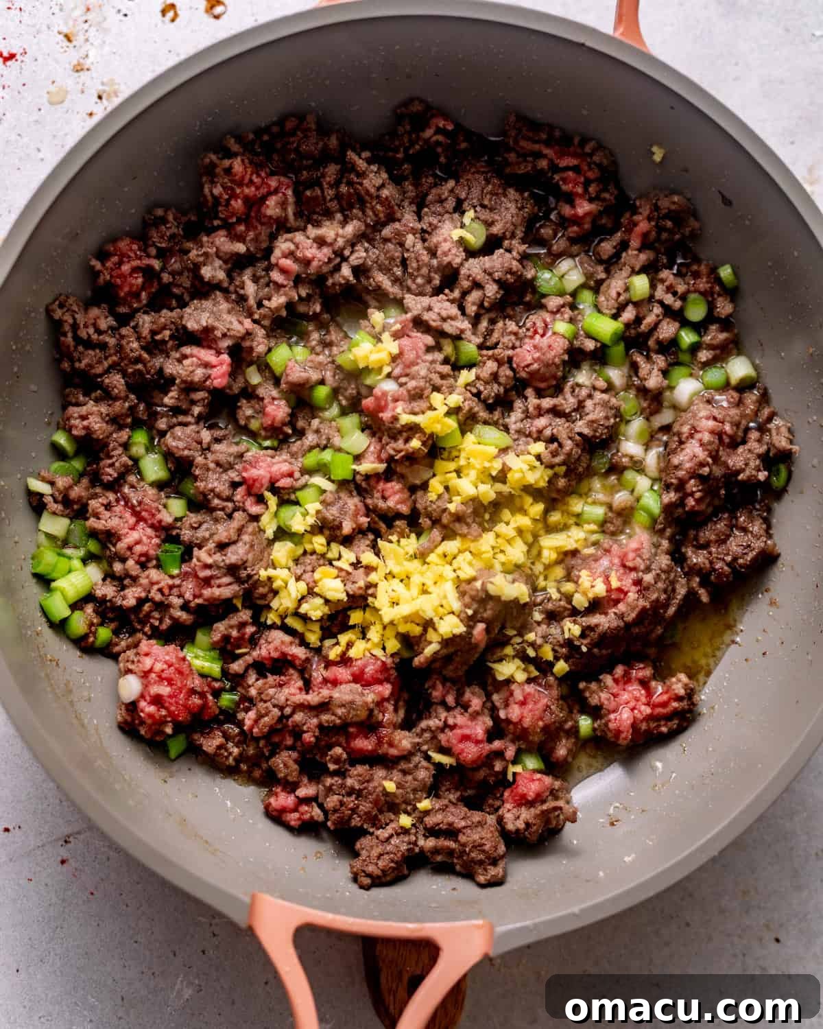 ground beef in a skillet with garlic, ginger, and scallions.