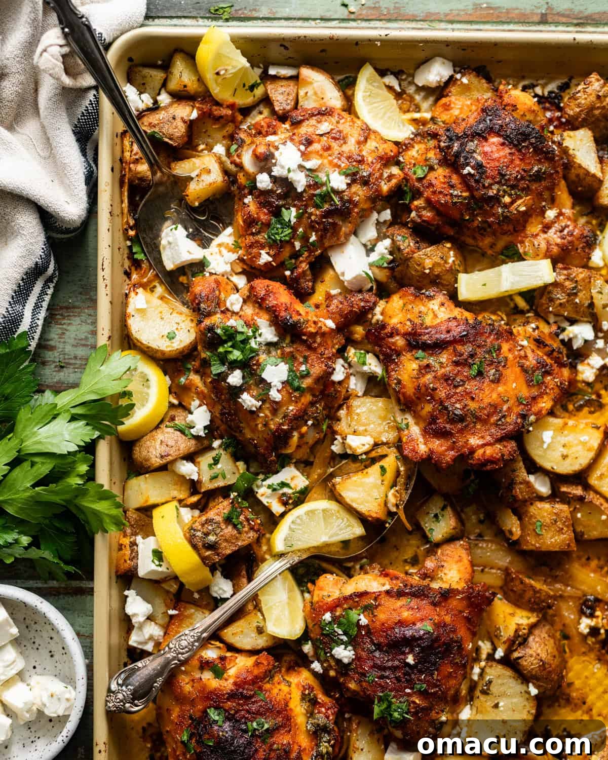 sheet pan chicken thighs and potatoes on a baking sheet with serving forks and garnished with feta and fresh parsley.