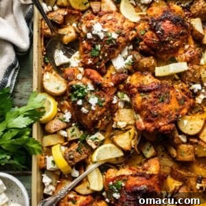sheet pan chicken thighs and potatoes on a baking sheet with serving forks and garnished with feta and fresh parsley.