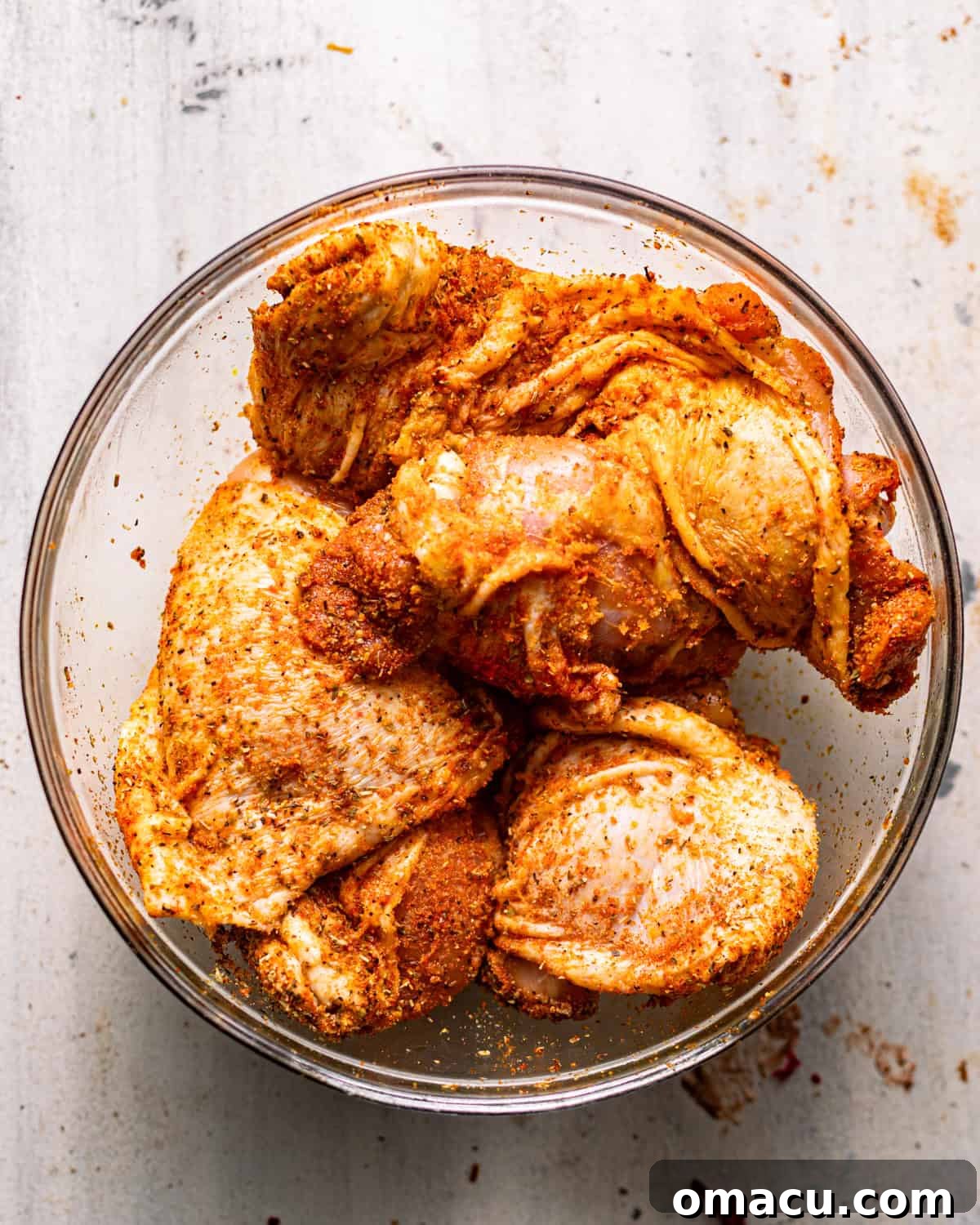 chicken in a bowl coated in olive oil and seasonings.
