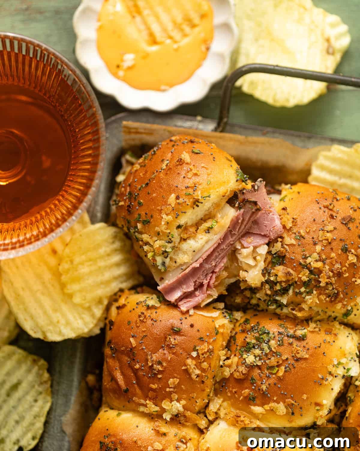 Reuben sliders arranged appealingly on a serving tray, accompanied by a small bowl of Thousand Island dressing for dipping and a side of crispy potato chips, showcasing their golden-brown tops and perfectly melted cheese.