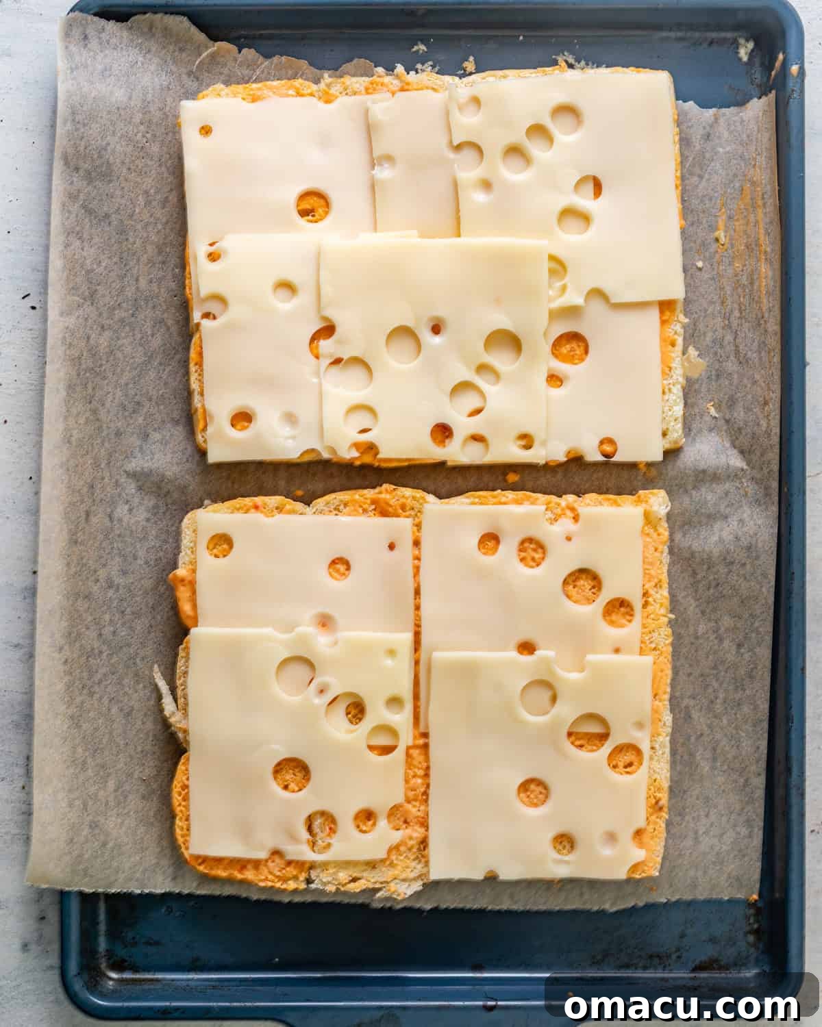 Hawaiian rolls sliced in half horizontally, with a generous spread of Thousand Island dressing on the bottom half, and neatly arranged slices of Swiss cheese covering the surface.