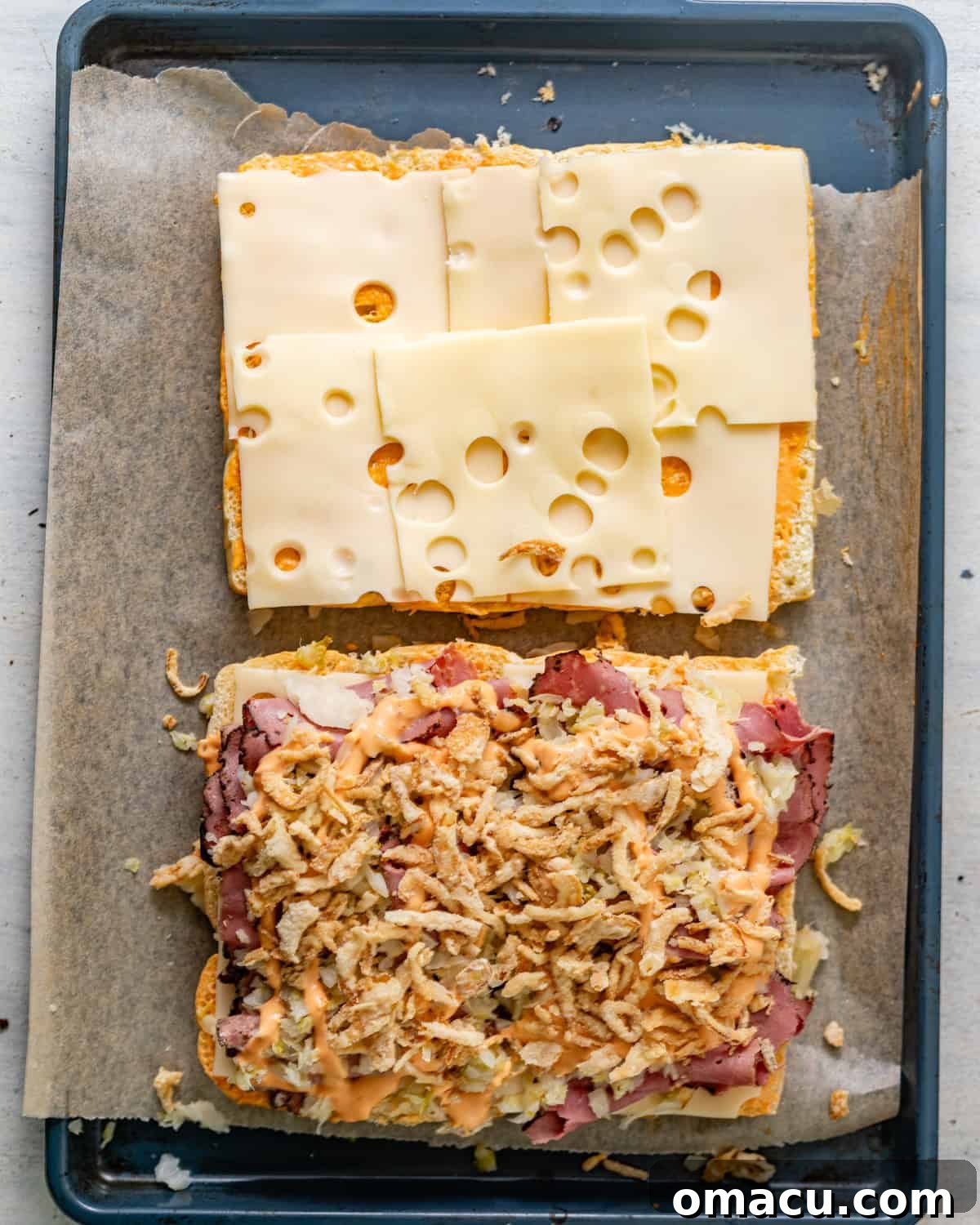 The bottom half of Hawaiian rolls layered with pastrami, followed by thoroughly drained sauerkraut, a second light drizzle of Thousand Island dressing, and a sprinkle of crispy French onions.