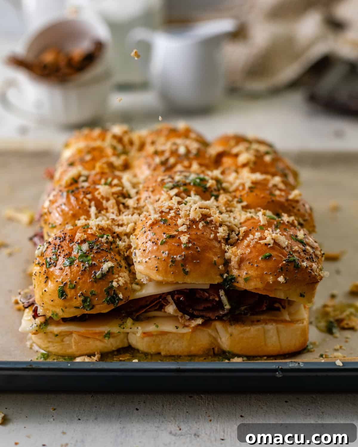 Fully assembled Reuben sliders resting on a baking sheet, with the remaining crispy French onions sprinkled on top of the garlic-buttered buns, awaiting their bake to golden perfection.