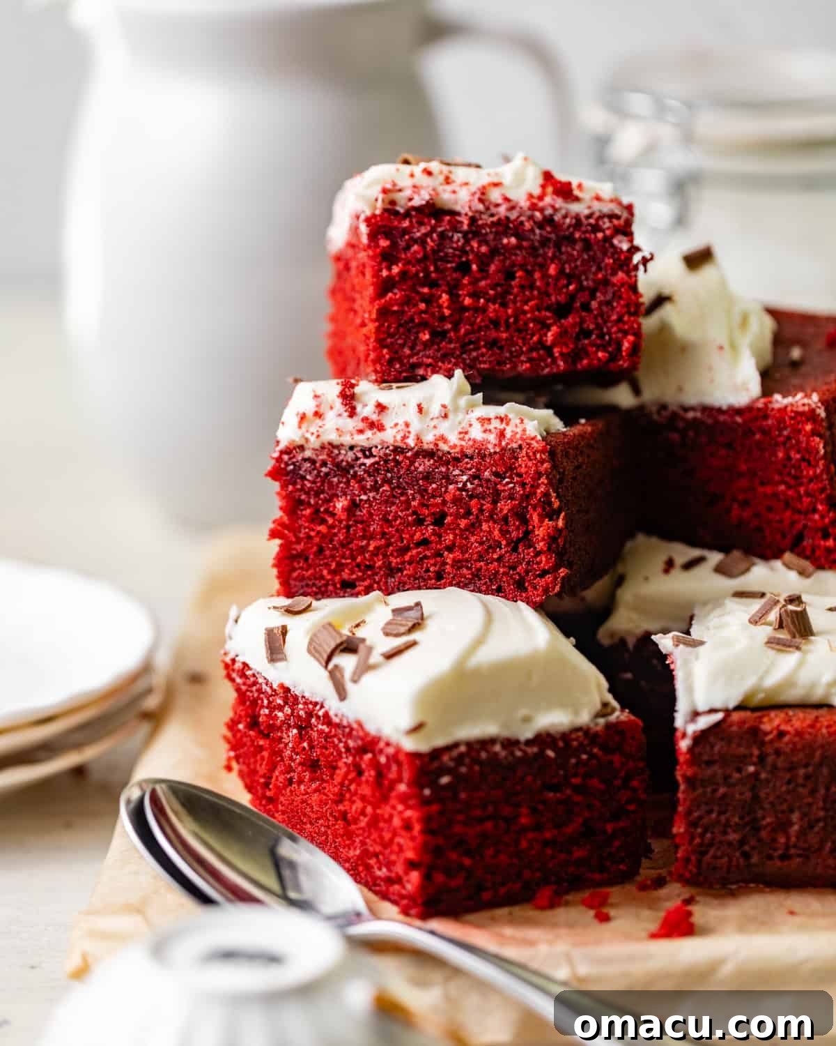 red velvet sheet cake sliced into pieces and stacked on top of each other, showcasing its vibrant color and thick cream cheese frosting.