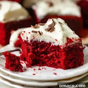 A tempting slice of red velvet cake on a cake plate, topped with smooth cream cheese frosting and chocolate shavings.