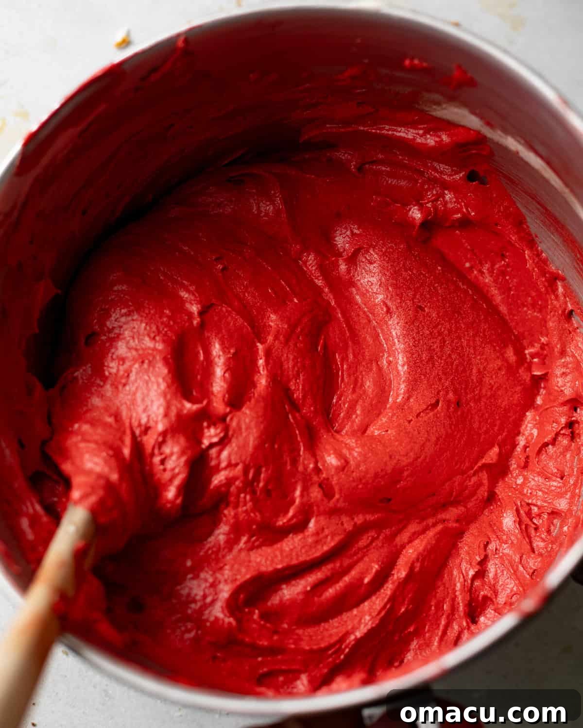 A vibrant red red velvet cake batter is shown in a mixing bowl, smooth and ready for baking.