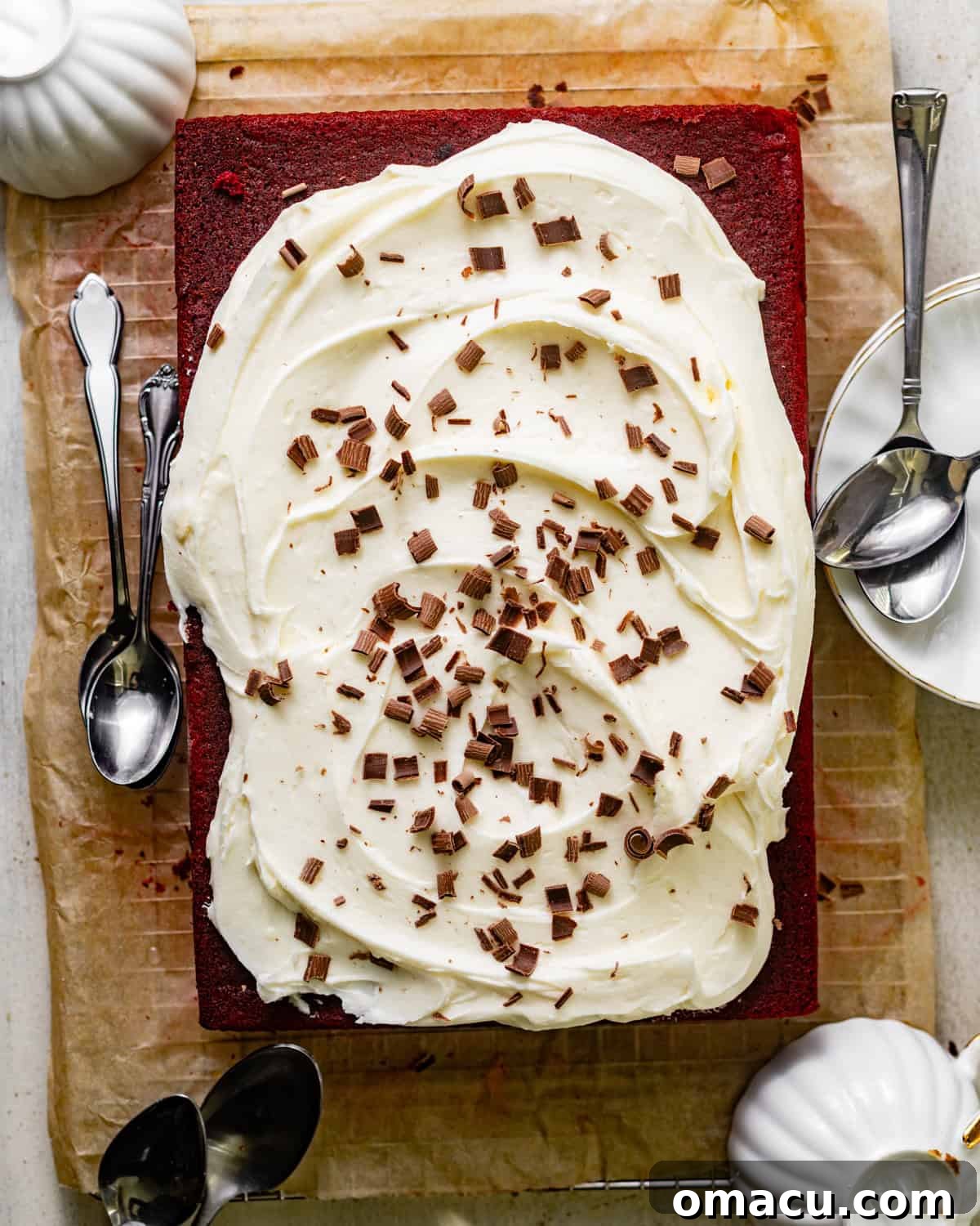 Overhead shot of a beautifully frosted red velvet sheet cake on parchment paper, adorned with delicate chocolate shavings.