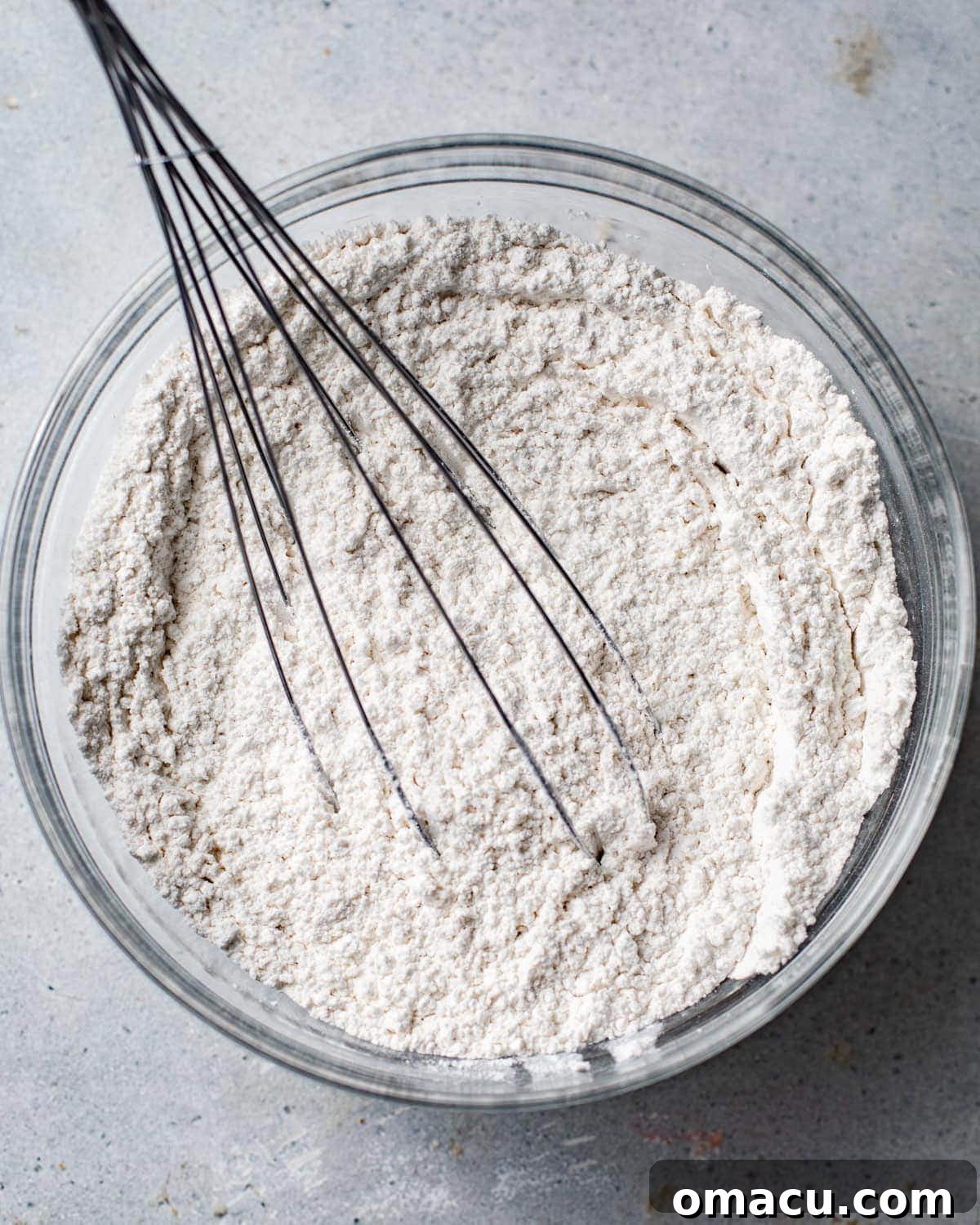 Dry ingredients, including cake flour, baking soda, and kosher salt, are whisked together in a large mixing bowl, ready for the next step in making the lemon ricotta pound cake.