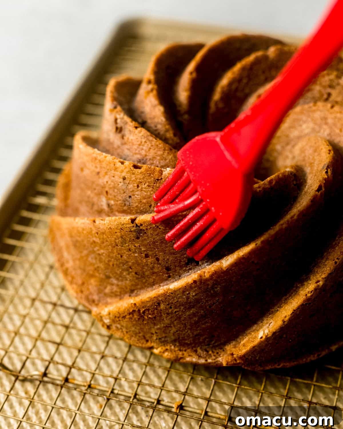 A warm, freshly baked bundt cake is shown on a wire rack as a pastry brush applies lemon simple syrup to its surface, enhancing moisture and flavor.