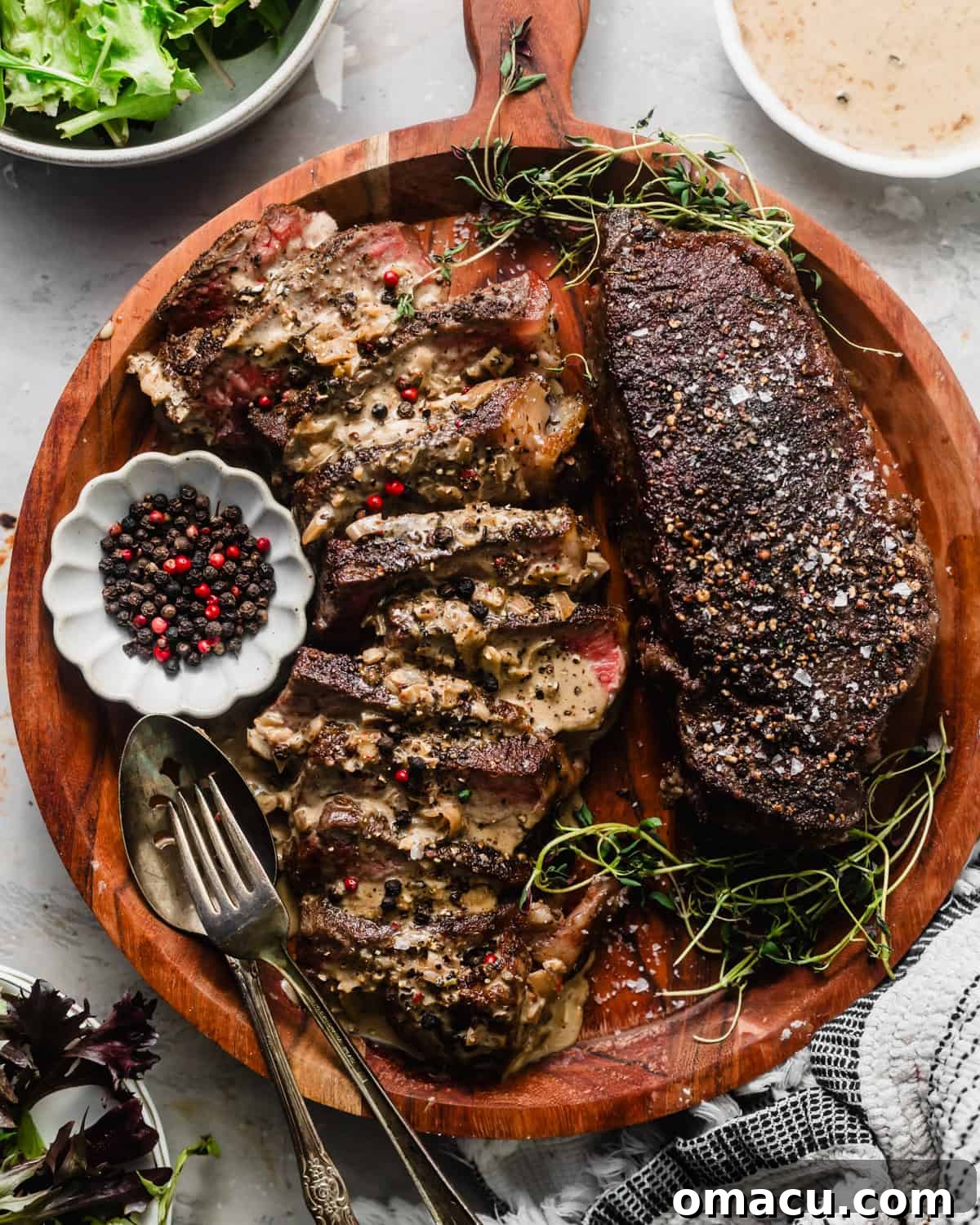Steak au poivre on a cutting board with peppercorns in a bowl and a fresh salad in a separate bowl, ready to be served.