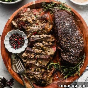 Steak au poivre on a cutting board with peppercorns in a bowl and salad in a separate bowl.