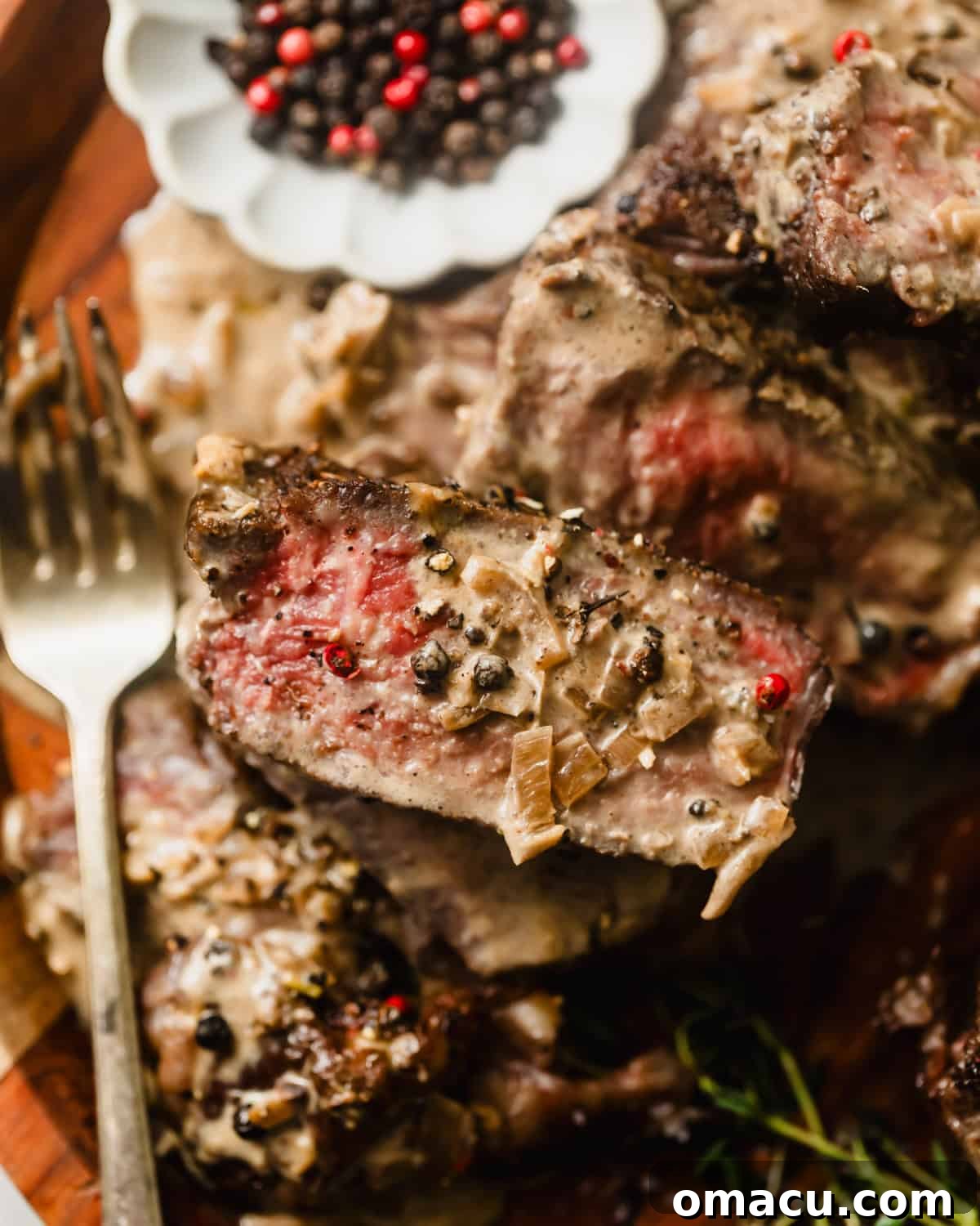 Sliced steak on a fork covered in au poivre sauce, highlighting the rich texture and delicious appeal.