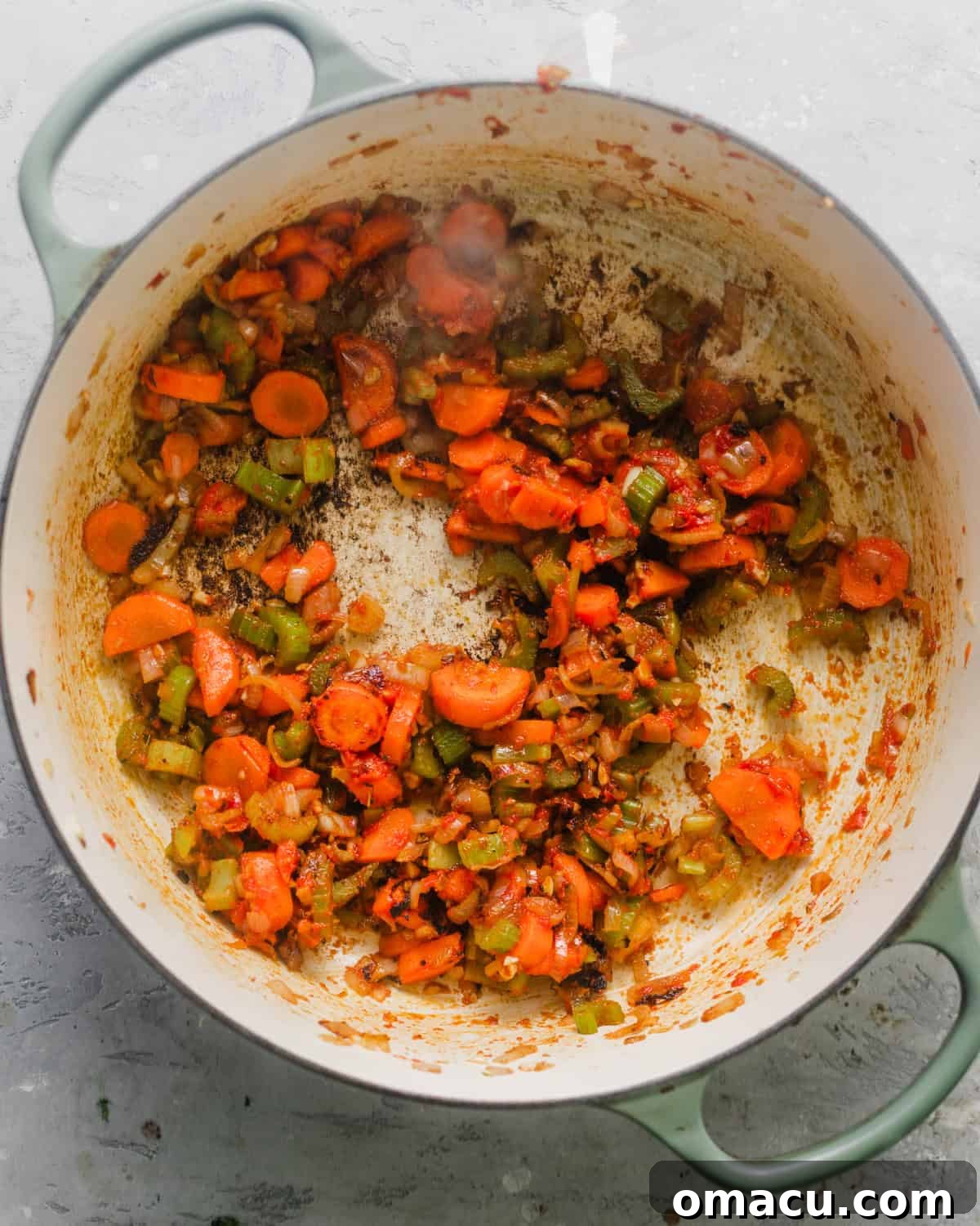 A pot on the stovetop filled with softened carrots, celery, shallots, garlic, and tomato paste, forming the flavorful base of the bisque.