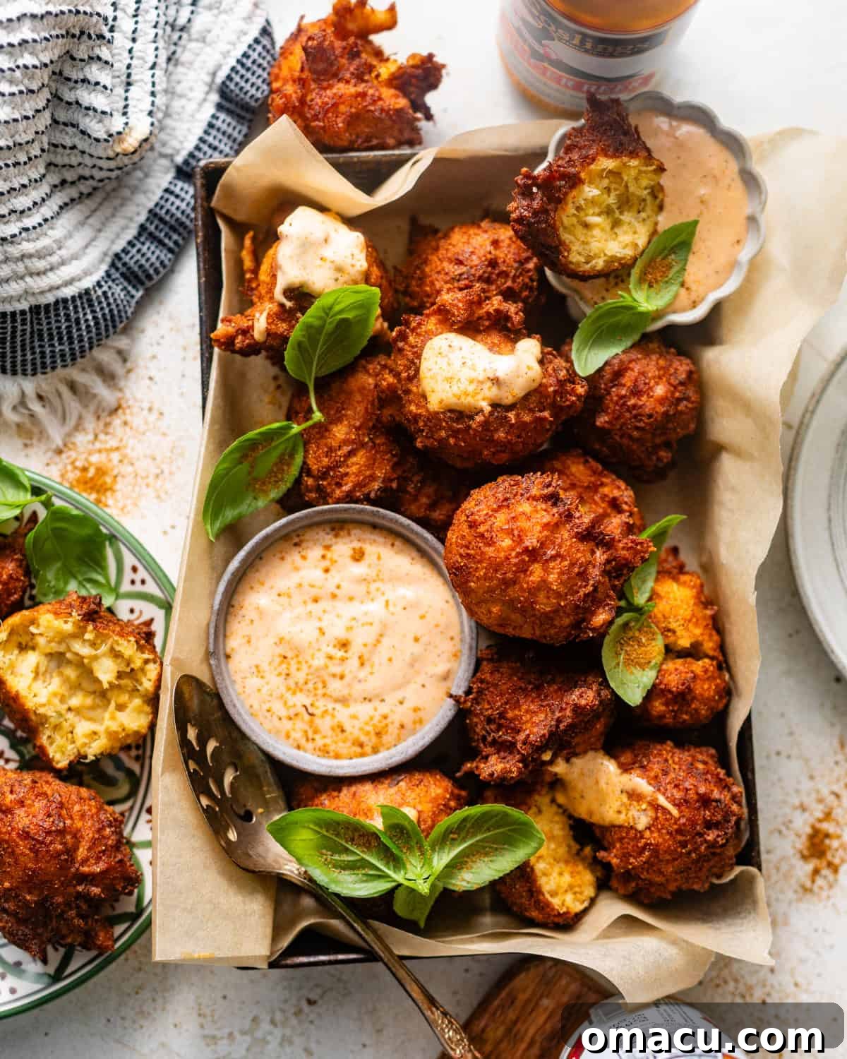 Golden-brown crab beignets arranged in a rustic basket lined with parchment paper, accompanied by a small bowl of zesty remoulade sauce.