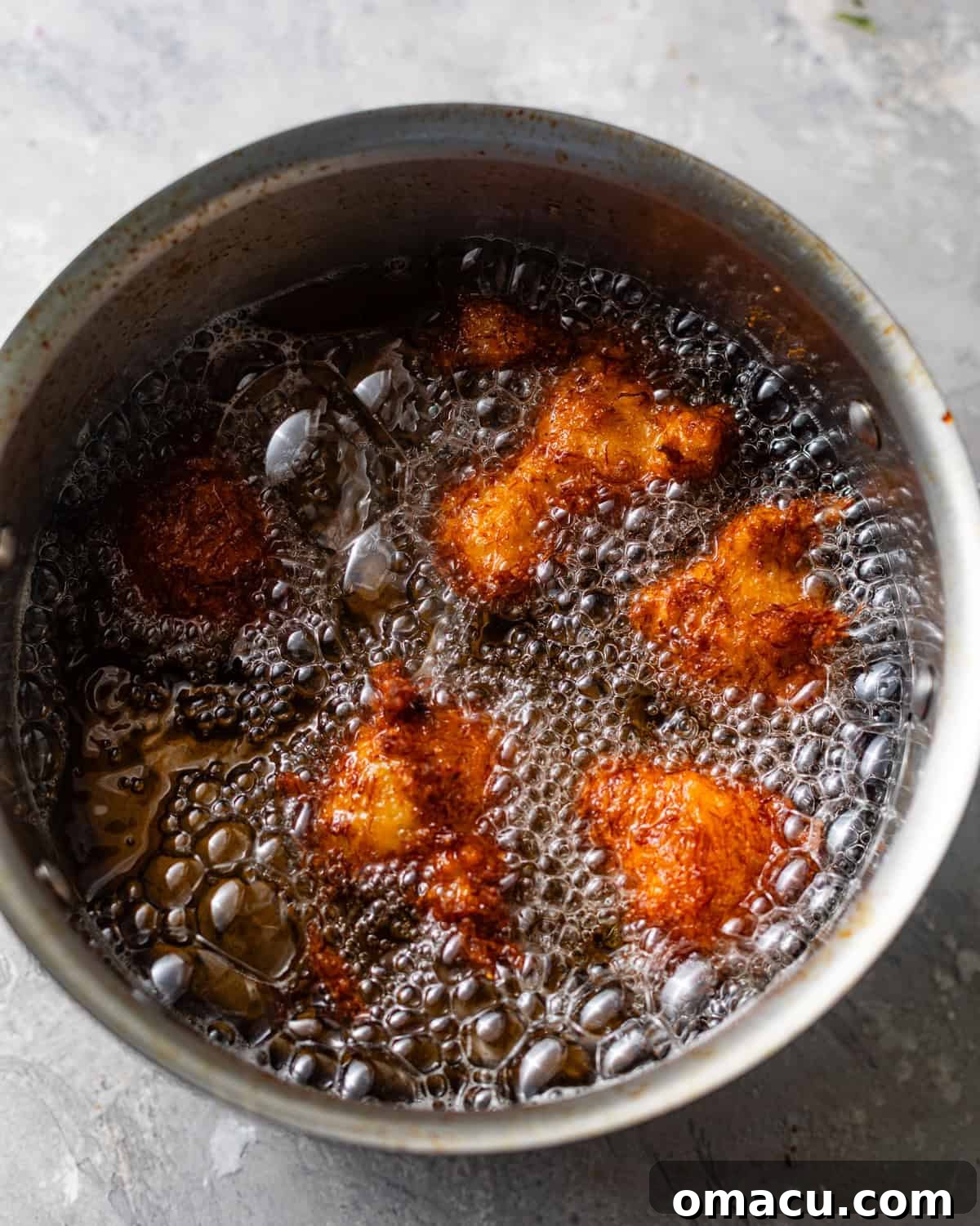 Crab beignets frying to a golden brown in hot oil within a deep pot.