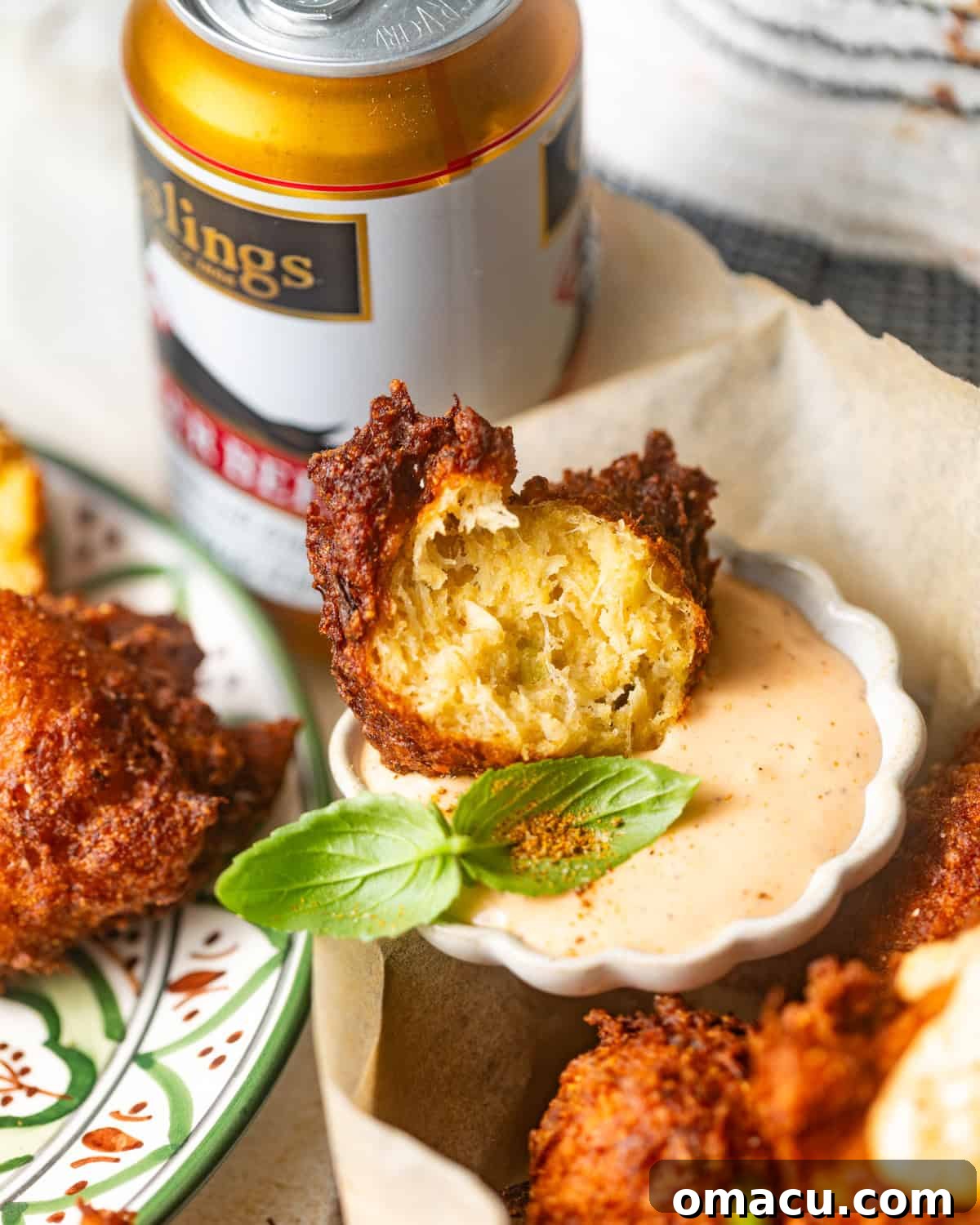 A golden-brown crab beignet cut in half, revealing its fluffy interior and chunks of crab meat, perfectly dipped into a dollop of remoulade sauce.