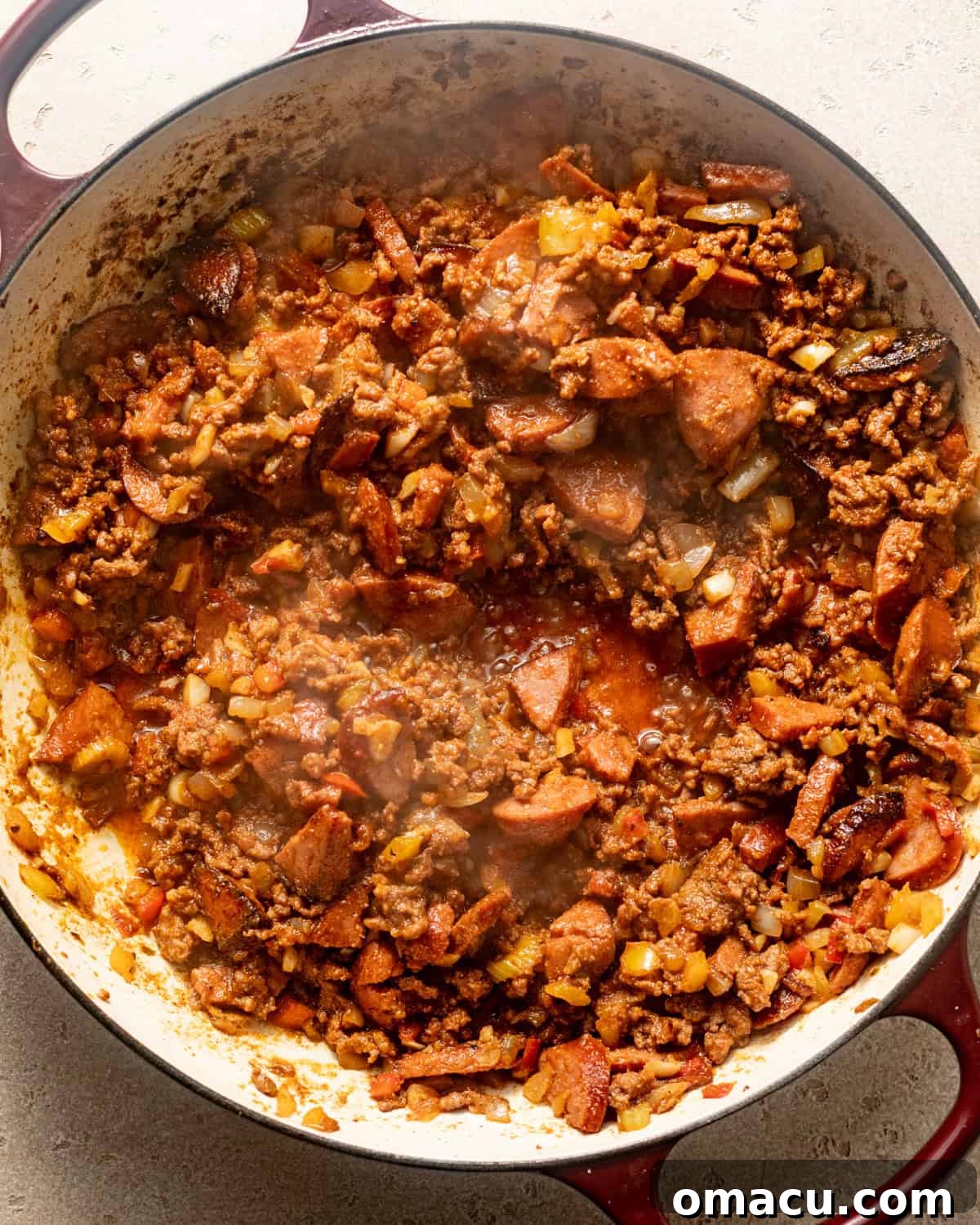 sausage and vegetables in a pot with ground beef, seasonings, and tomato paste.