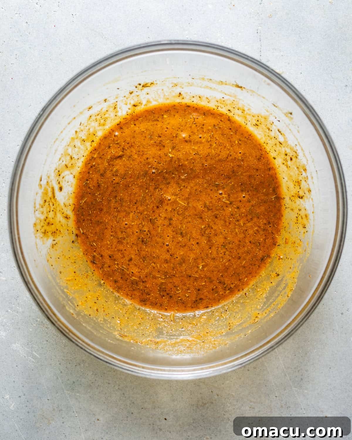A bowl containing a whisked mixture of milk, beef bouillon, eggs, Dijon mustard, ketchup, Worcestershire sauce, and various seasonings, ready for breadcrumbs and ground beef.