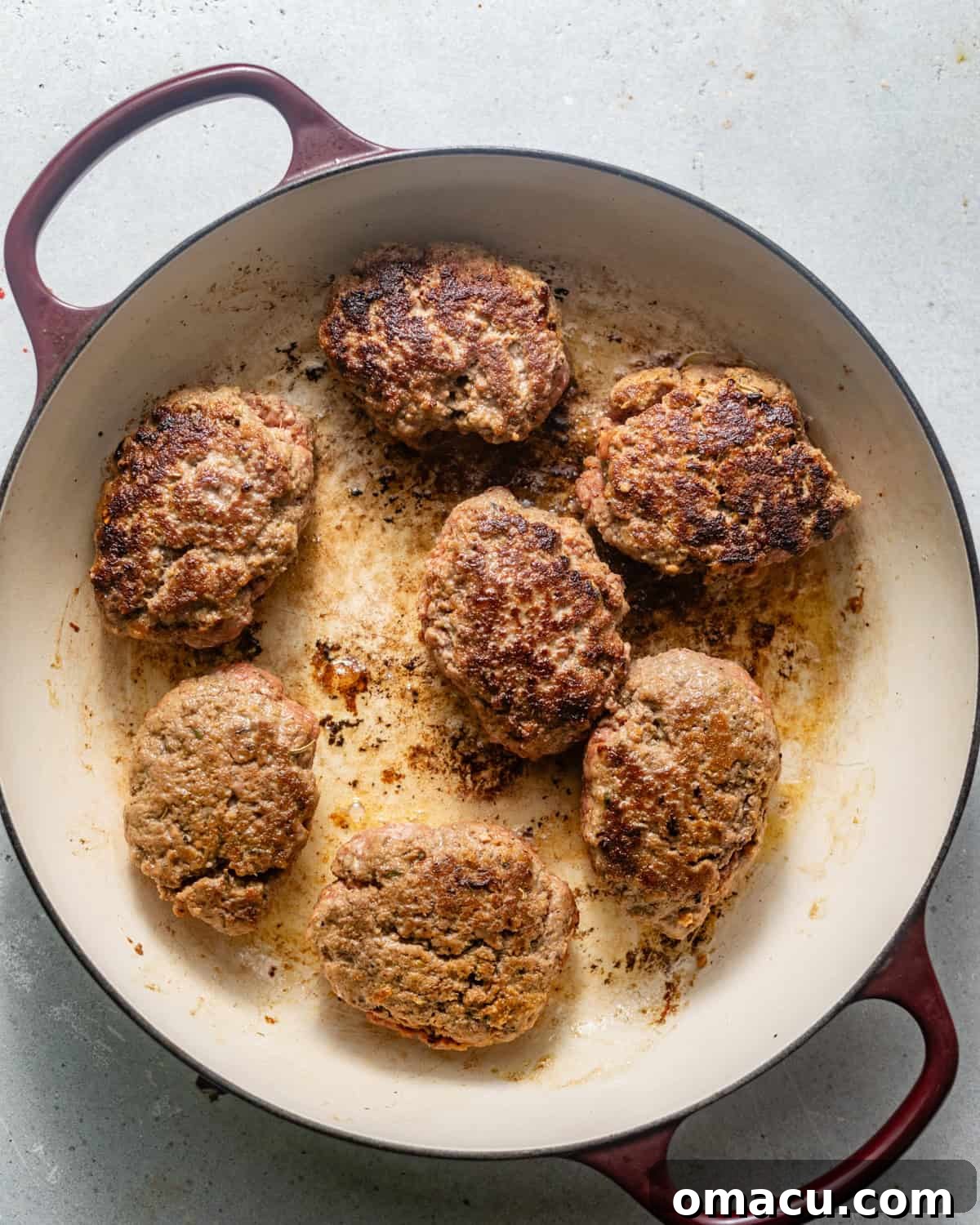 Three seared, golden-brown hamburger steaks in a hot cast-iron pan, showing a beautiful crust.