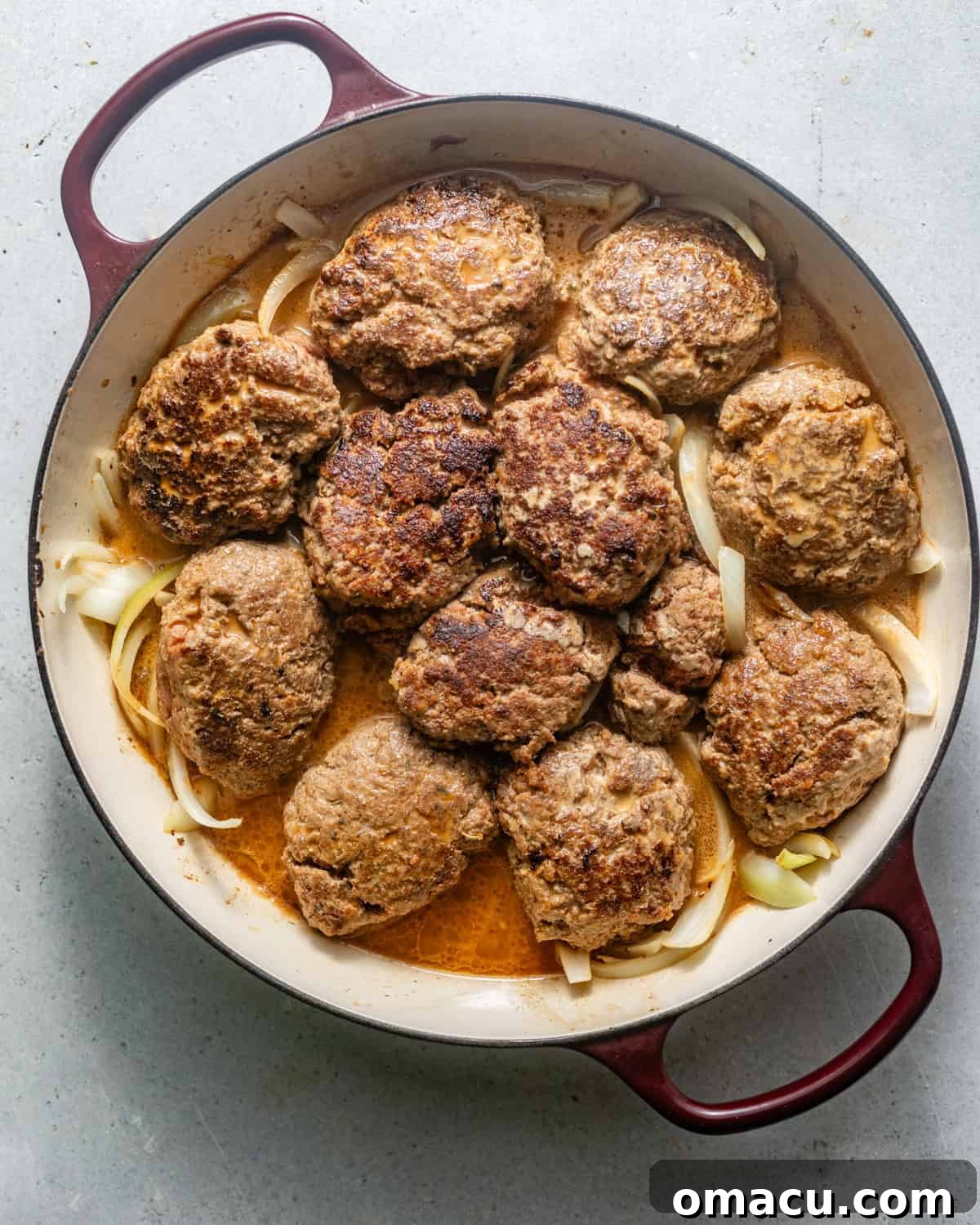 Hamburger steaks nestled in a pan with sautéed onions, garlic, and rich brown gravy, ready for baking.