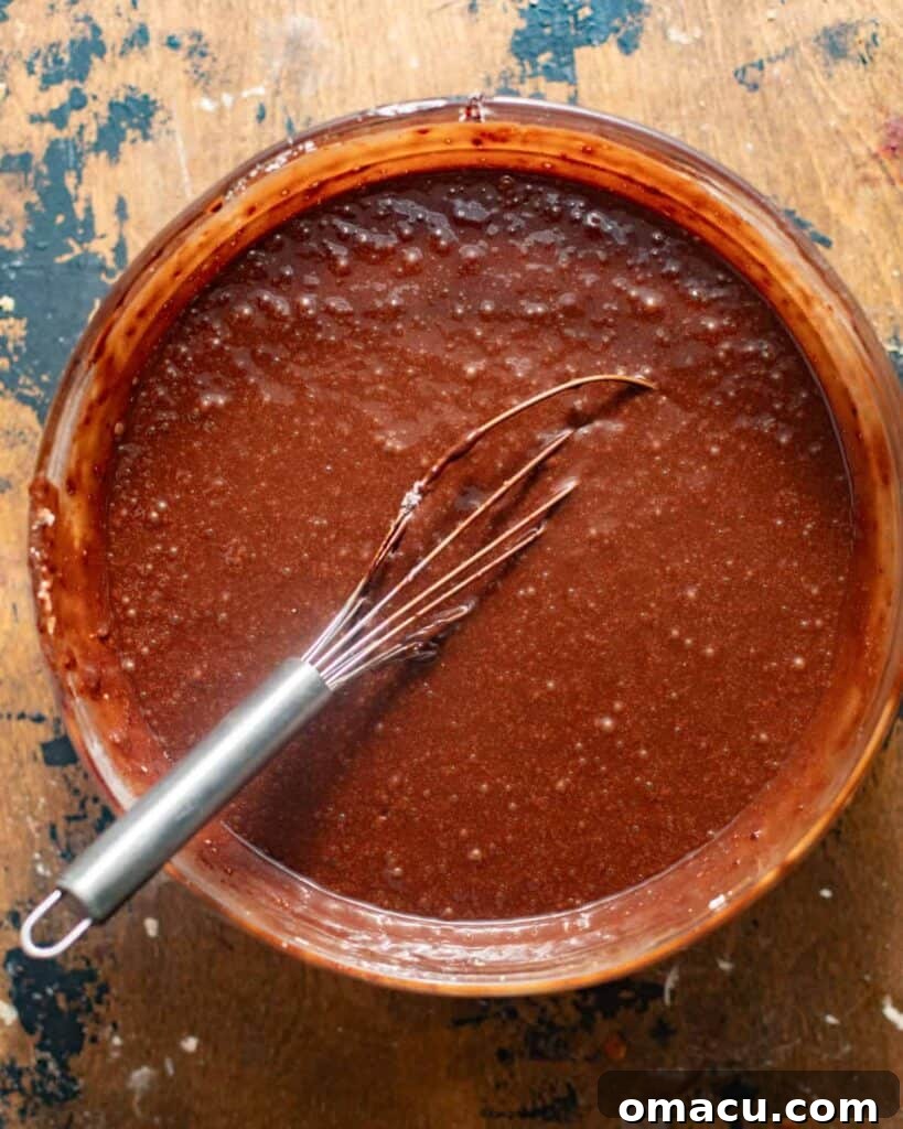 Smooth chocolate snack cake batter being whisked in a large mixing bowl, ready for baking.