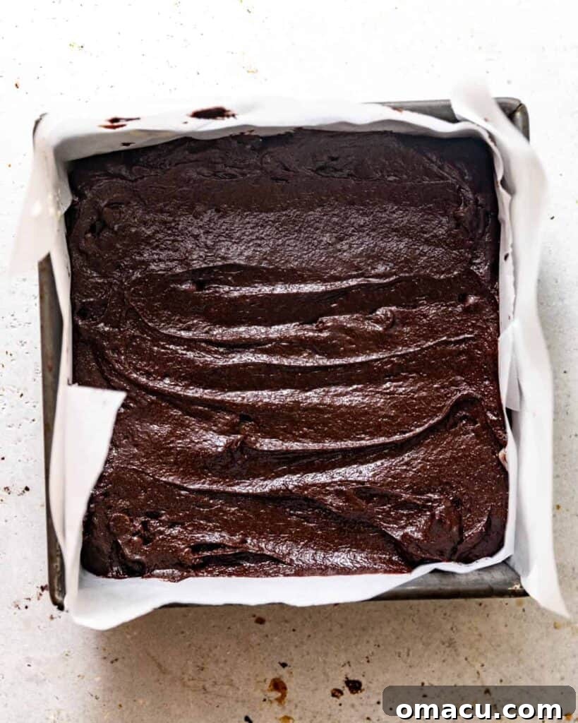 Rich chocolate snack cake batter poured into an 8x8 square baking dish, ready for the oven.
