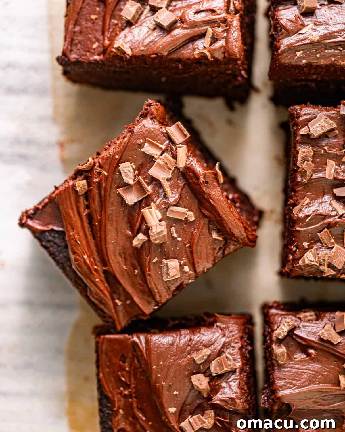 An inviting overhead shot of a freshly baked chocolate snack cake, topped with a luscious ganache, sitting on a piece of parchment paper.