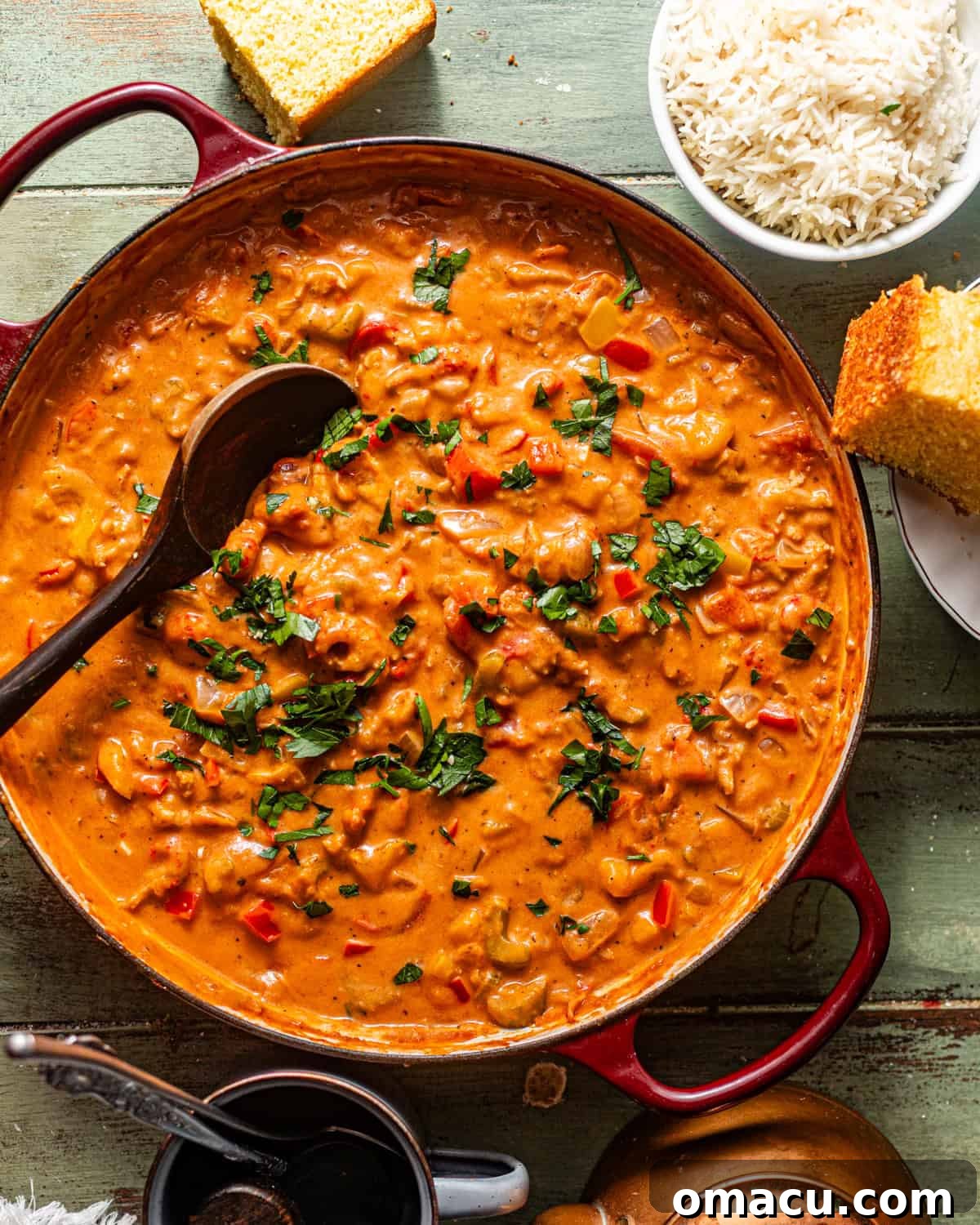 A wooden spoon stirring vibrant orange crawfish étouffée in a heavy-bottomed pot, showing the rich, thick consistency of the sauce.