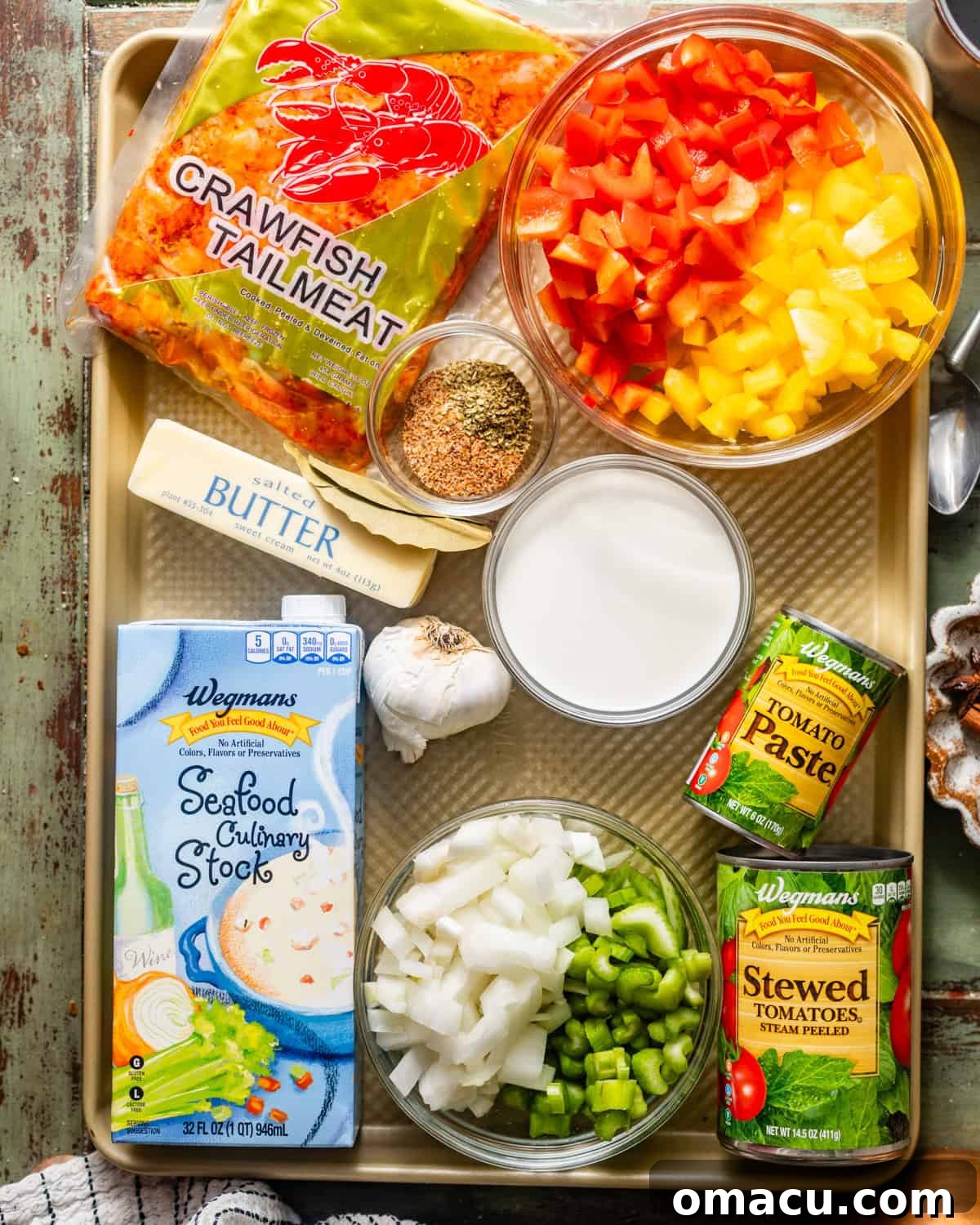 A vibrant flat lay showcasing all the fresh and pre-packaged ingredients needed to make crawfish étouffée, including pre-cooked crawfish tail meat, diced bell peppers, onions, celery, fresh garlic, tomato paste, stewed tomatoes, seafood stock, heavy cream, butter, flour, and a variety of Cajun seasonings.