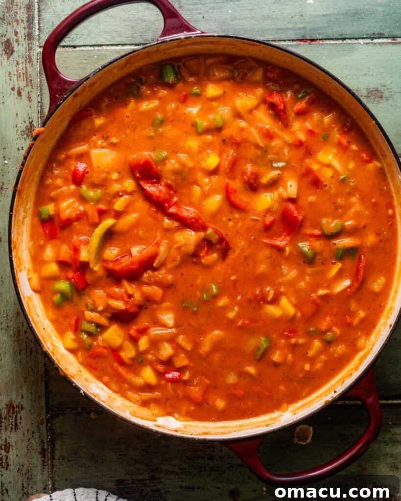 Stewed tomatoes and seafood broth simmering in a pot with the aromatics, creating a rich, thickening sauce for the étouffée.