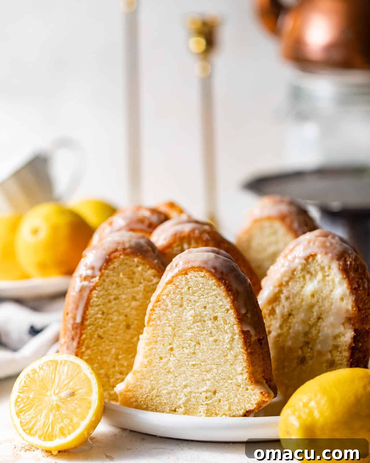 A perfectly sliced lemon buttermilk pound cake on a white plate, garnished with fresh lemon slices, showcasing its moist texture and golden-brown crust. This image highlights the delicious appeal of homemade lemon cake.