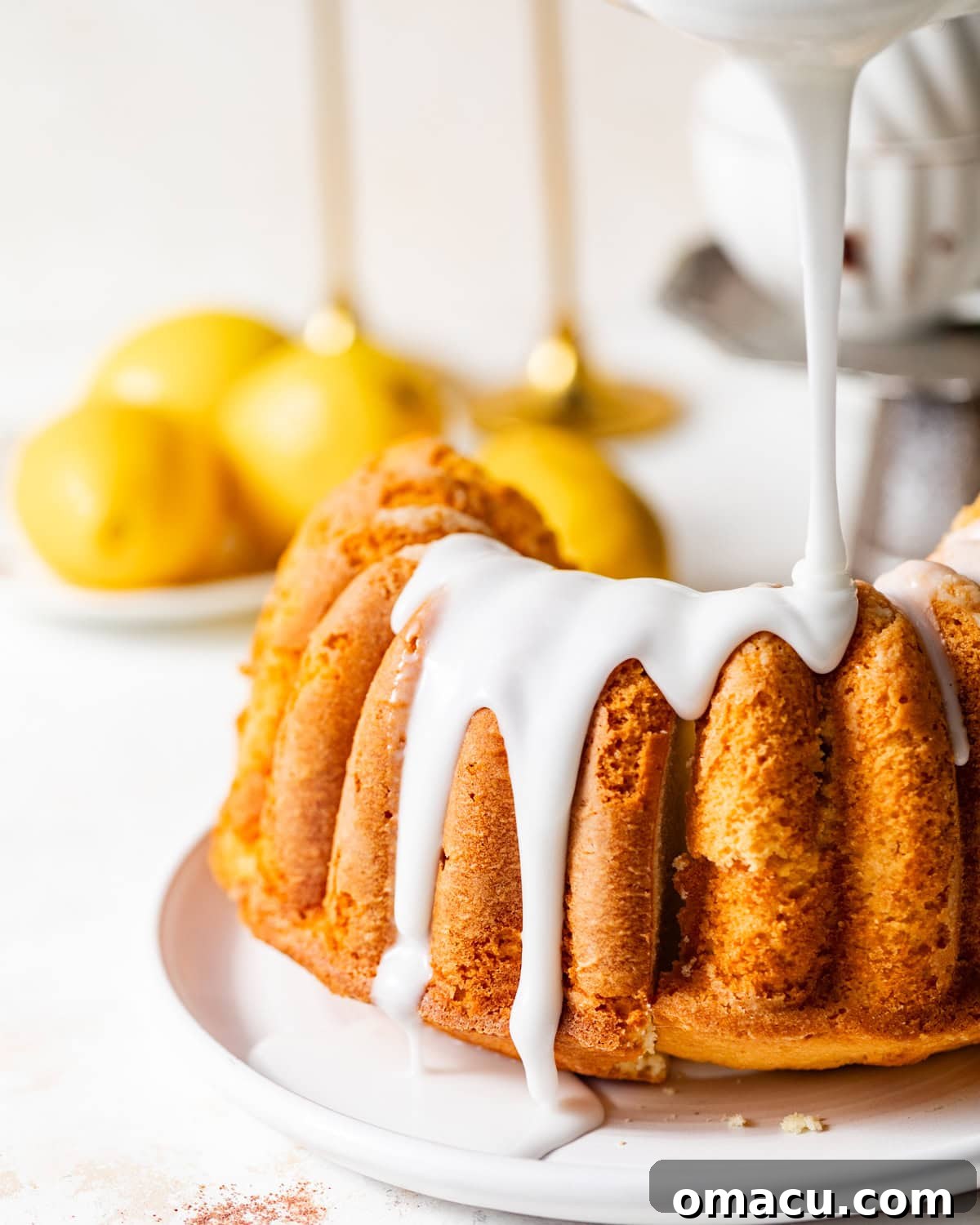 A luscious lemon glaze being drizzled artfully over a fully cooled lemon buttermilk pound cake, creating beautiful streaks and adding a final touch of sweetness and tang.