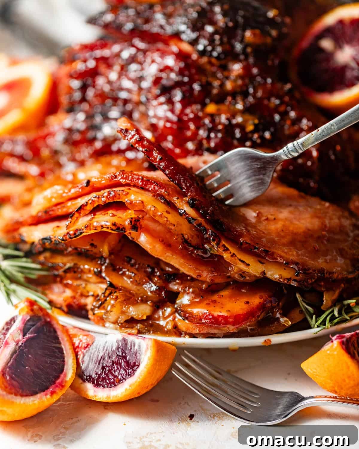 Perfectly sliced glazed ham on a fork, with vibrant orange slices arranged artfully beside it, highlighting the juicy texture.