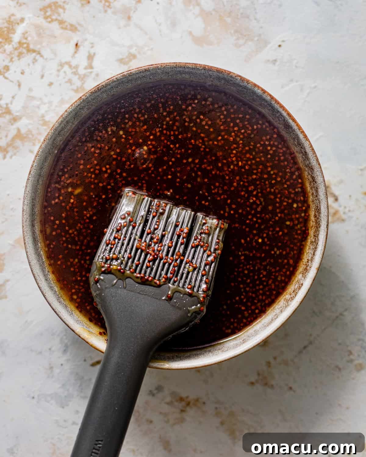 The glistening orange brown sugar glaze, thick and syrupy, rests in a bowl with a pastry brush, ready to be applied to the ham.
