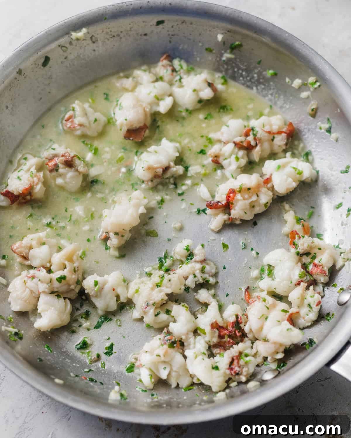 Chunks of lobster cooked in garlic butter in a pan.