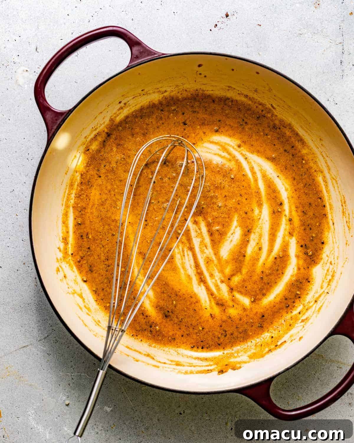 A roux and seasonings being whisked in a skillet.
