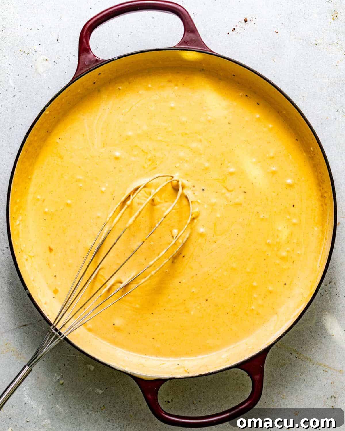 Creamy cheese sauce in a skillet with a whisk.