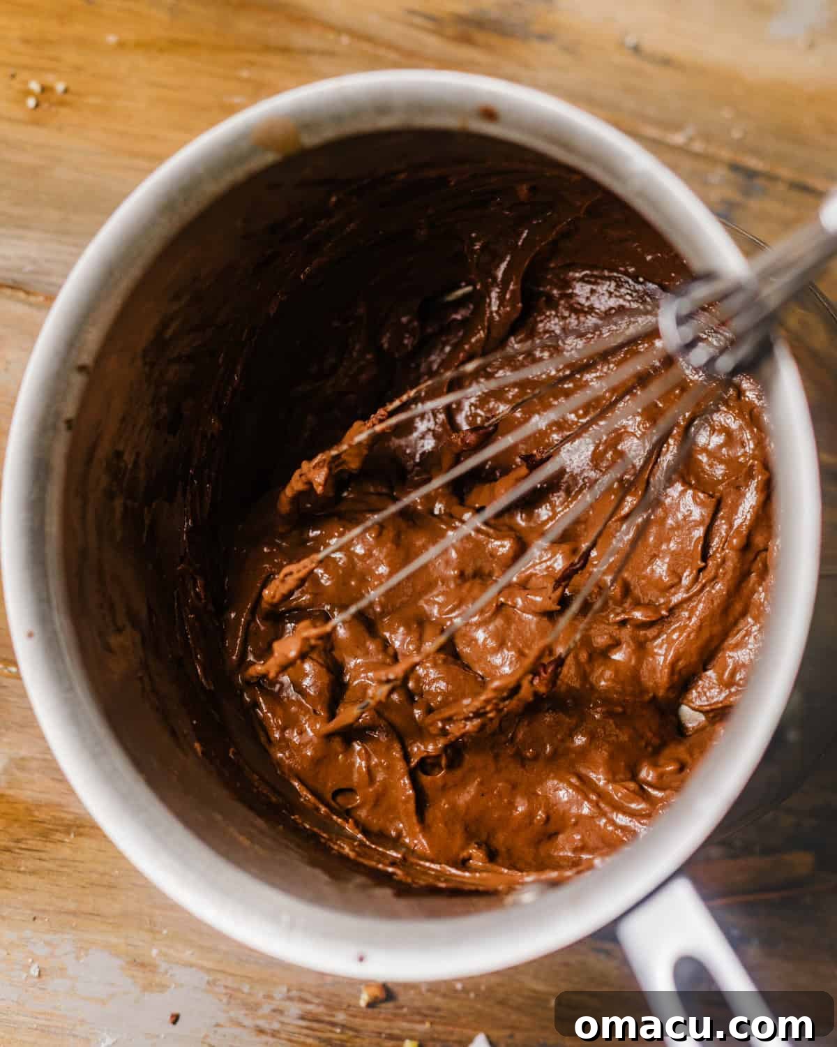 Melted butter, chocolate chips, and heavy cream combining in a saucepan with a whisk.