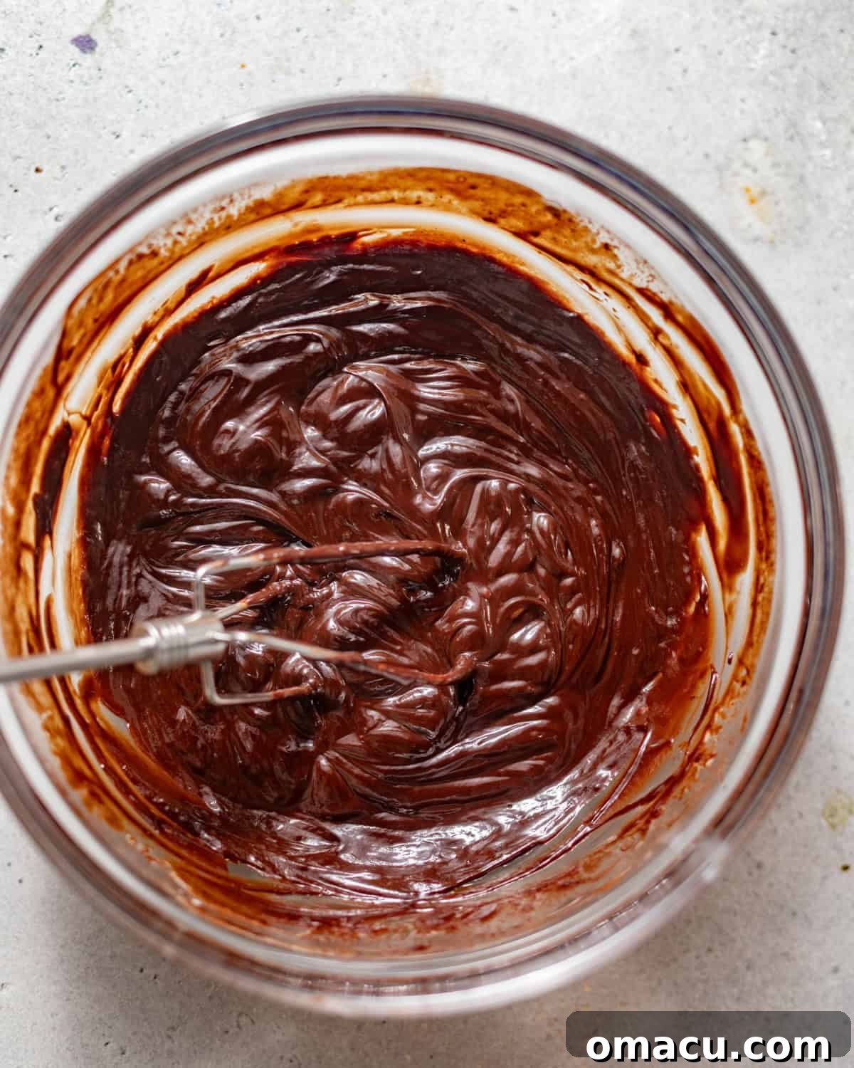 Chocolate mixture with corn syrup, powdered sugar, cocoa powder, and vanilla bean paste being whisked in.