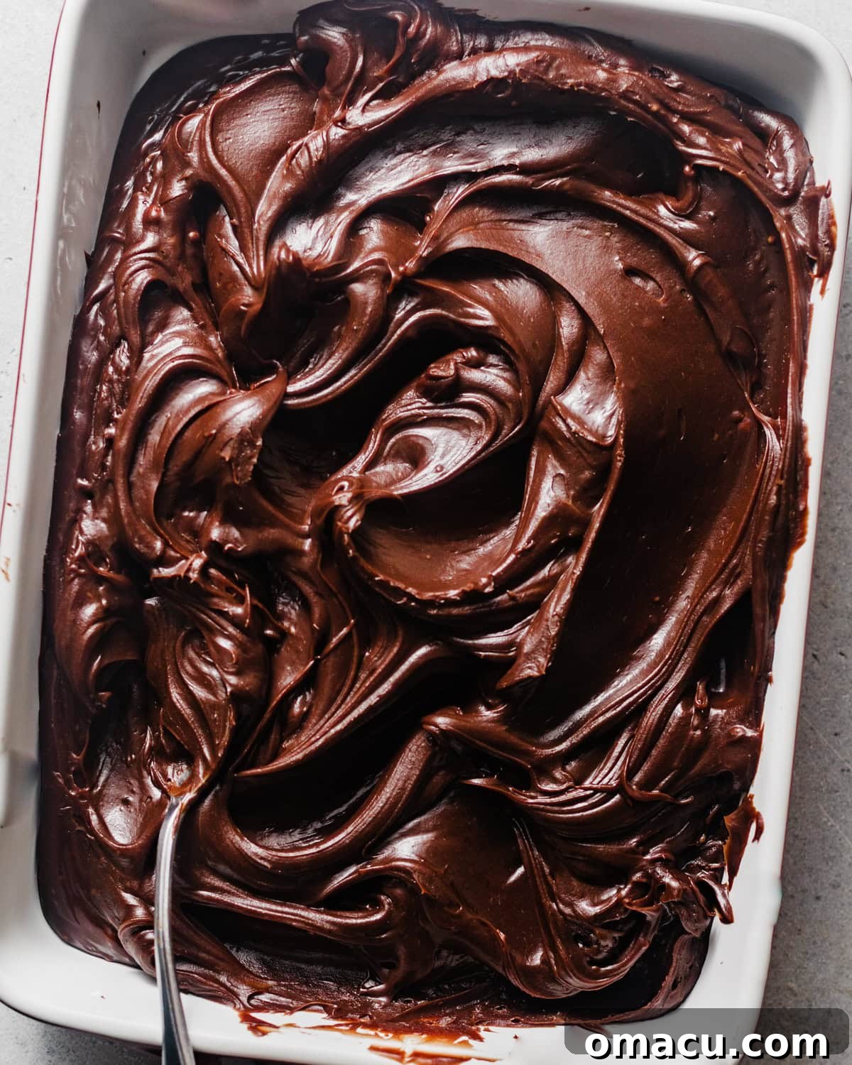 Chocolate fudge frosting poured into a baking dish to cool, covered with plastic wrap.