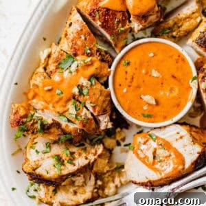 sliced baked pork tenderloin on a plate with cajun sauce and fresh parsley on top.